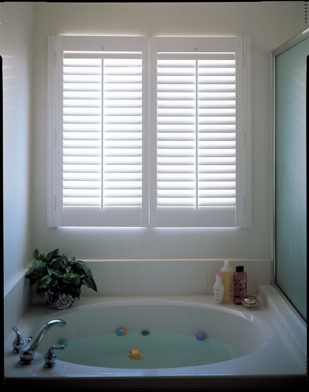 White bathroom with a jacuzzi tub. Shutters cover the window.