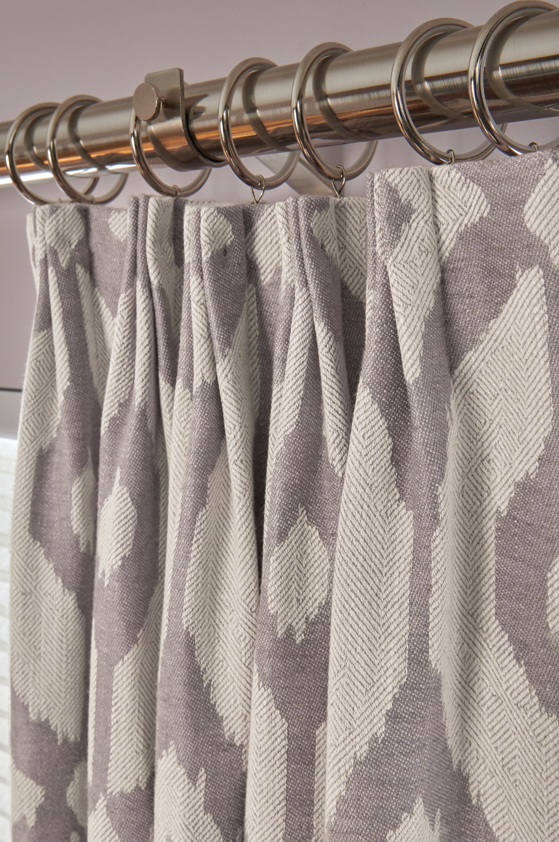 Gray and white patterned curtains with pleats hanging from a silver rod with rings.