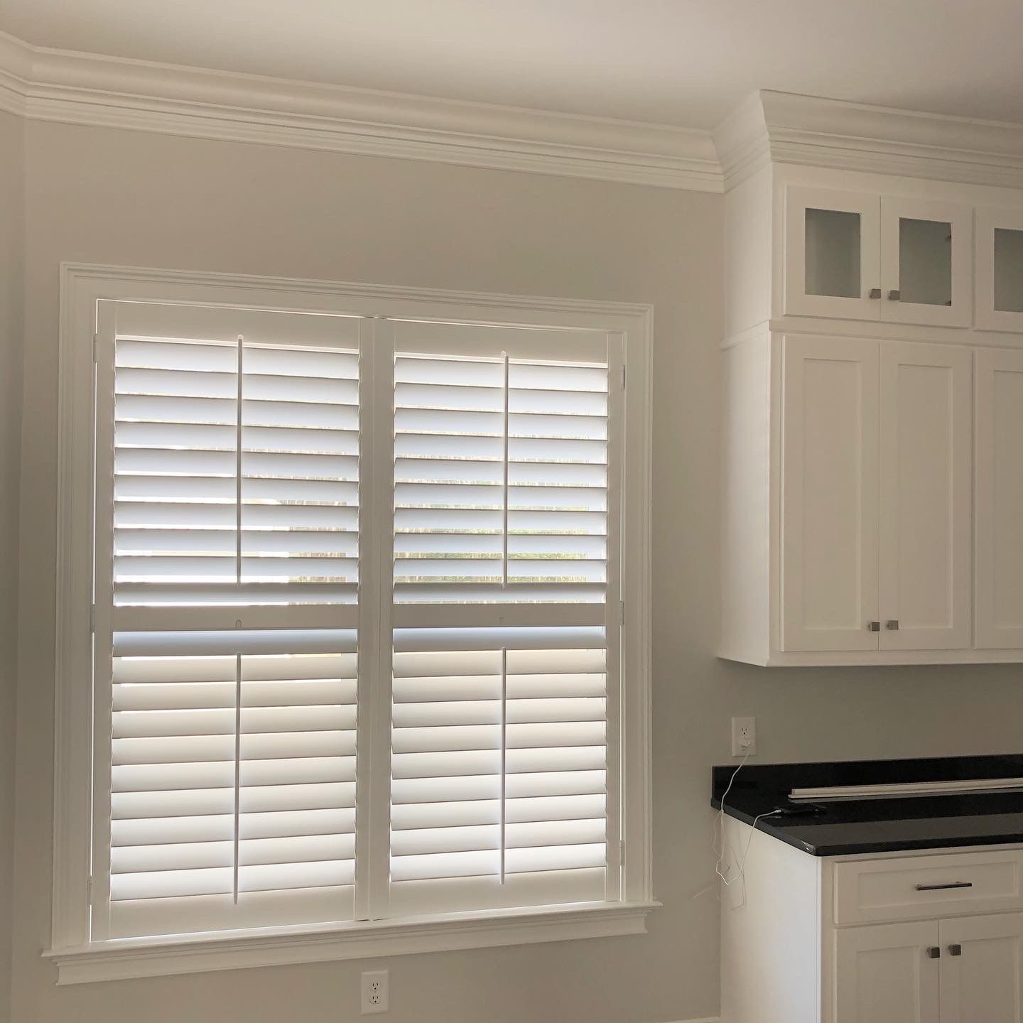 White shutters on a window in a kitchen, next to white cabinets.