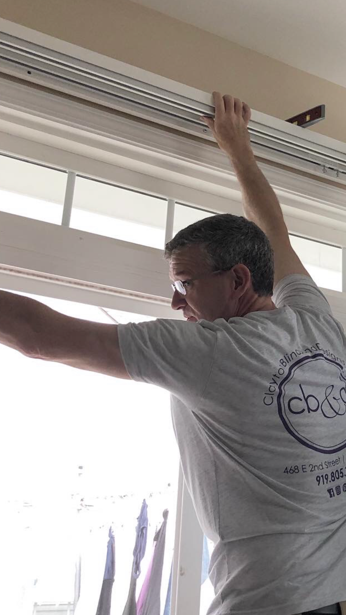 Man installing a window shade, reaching up. White shirt, interior shot.
