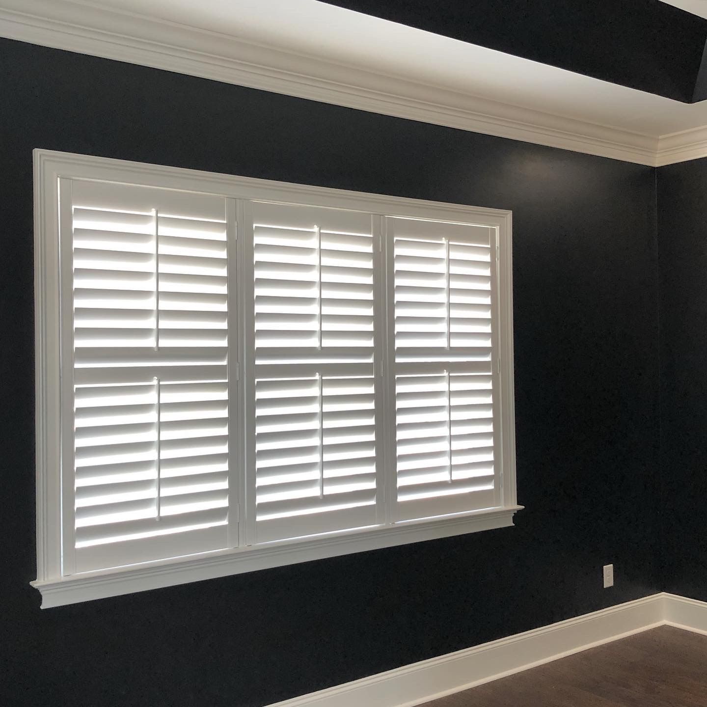 White shuttered window in black-painted room with white trim and ceiling.