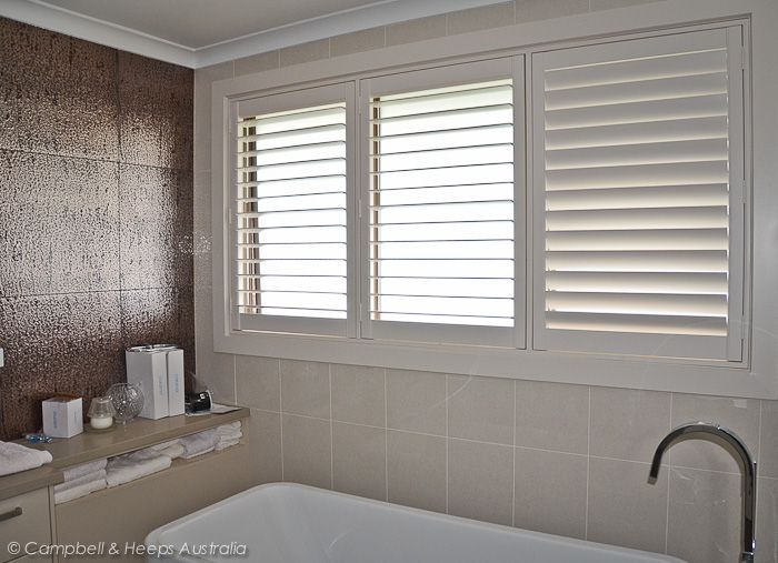 Bathroom with white shutters over windows, bathtub, and brown-tiled wall.