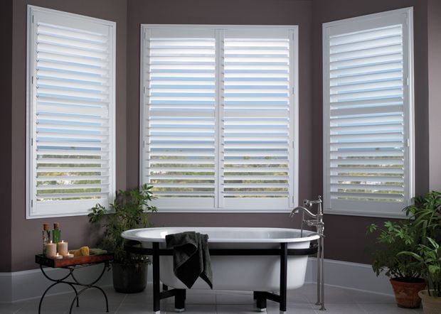 Bathroom with white shuttered windows, freestanding tub, and plants.