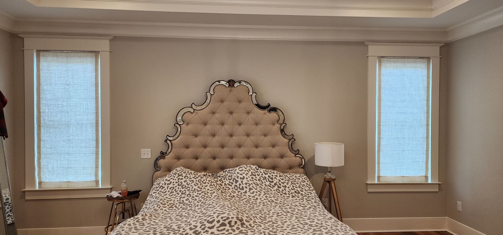 Bedroom with a tufted headboard, patterned bedding, and two windows with blinds.