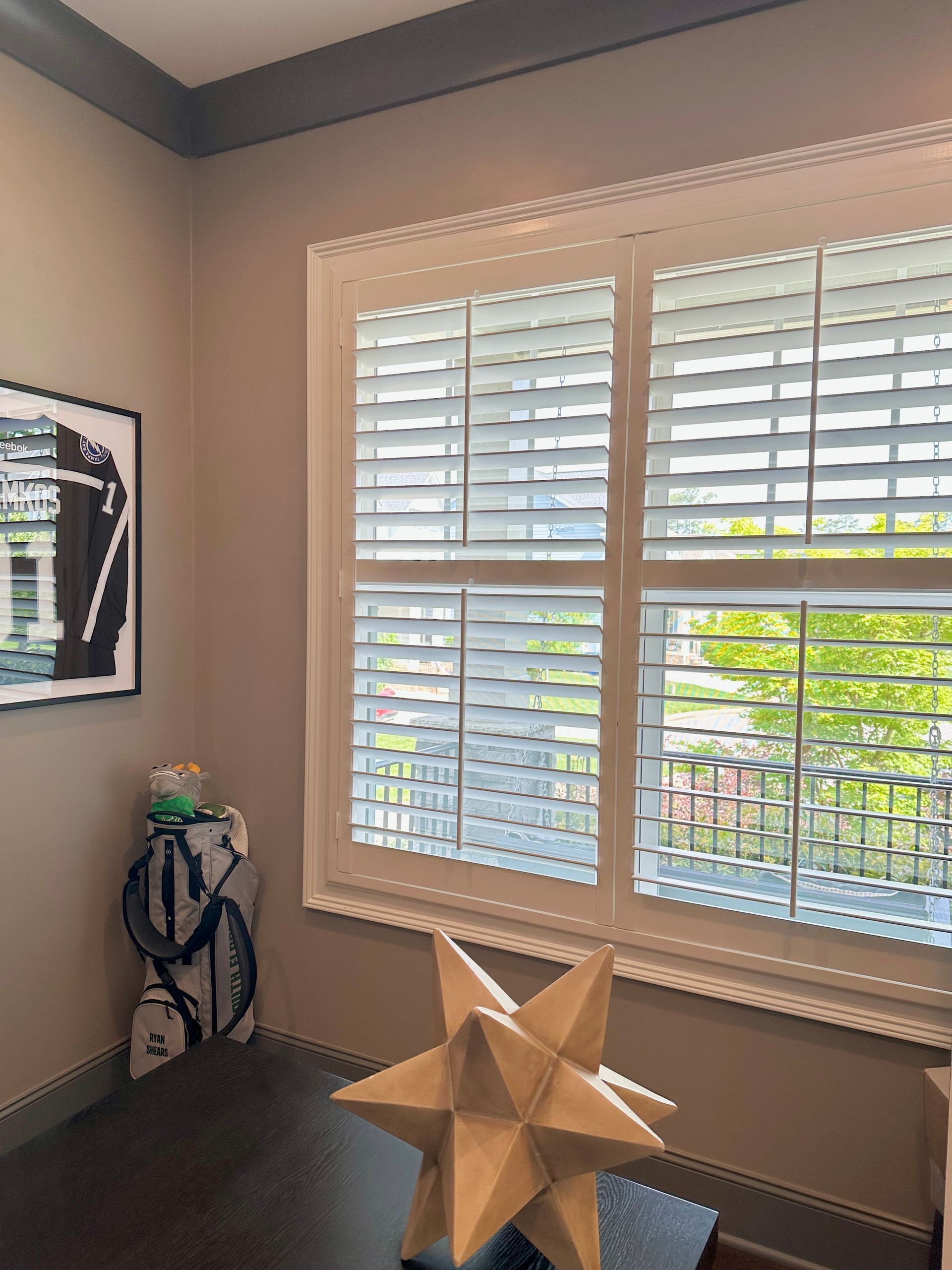 Room interior with window shutters; artwork on wall. Neutral colors, natural light. Desk with geometric star.