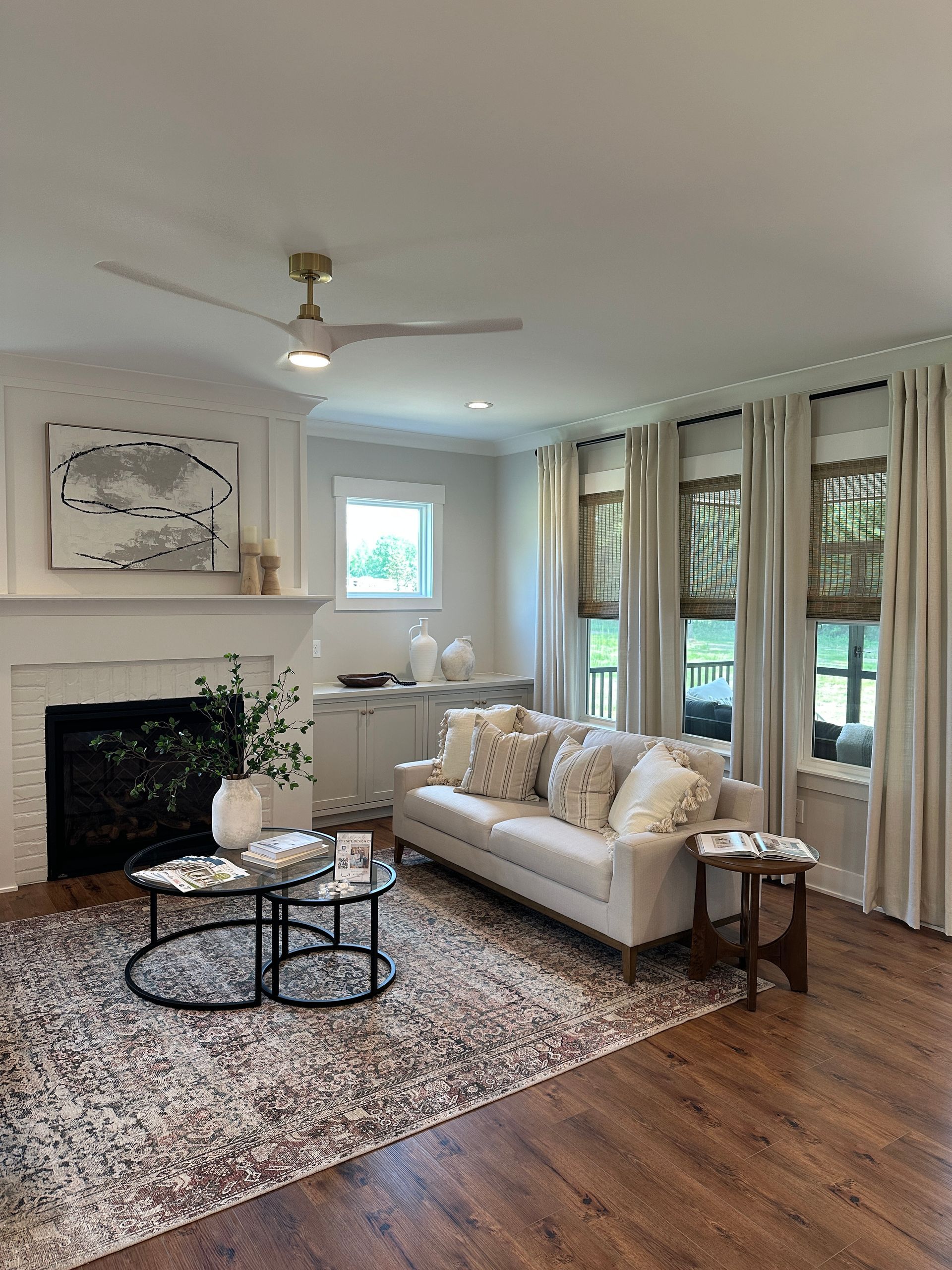 Living room with fireplace, white sofa, patterned rug, wooden floors, and sheer curtains.