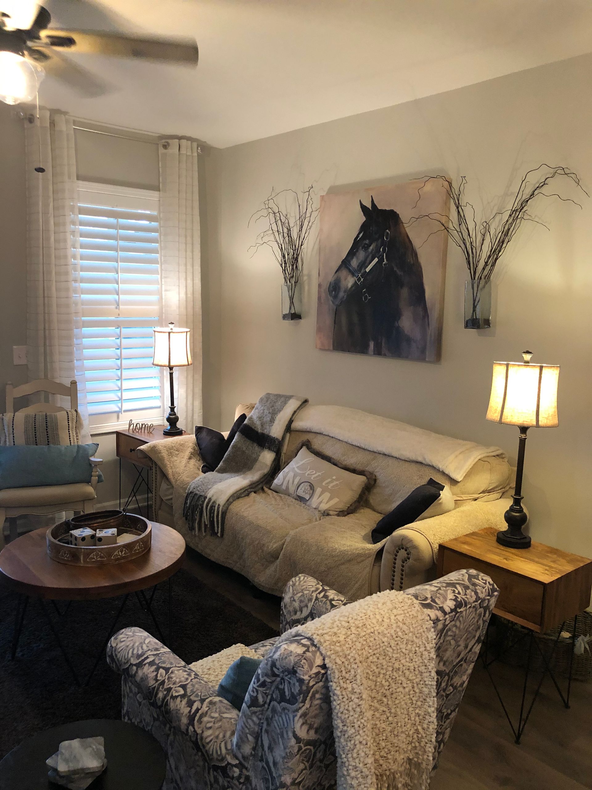 Living room with beige sofa, horse painting, lamps, and a round coffee table.
