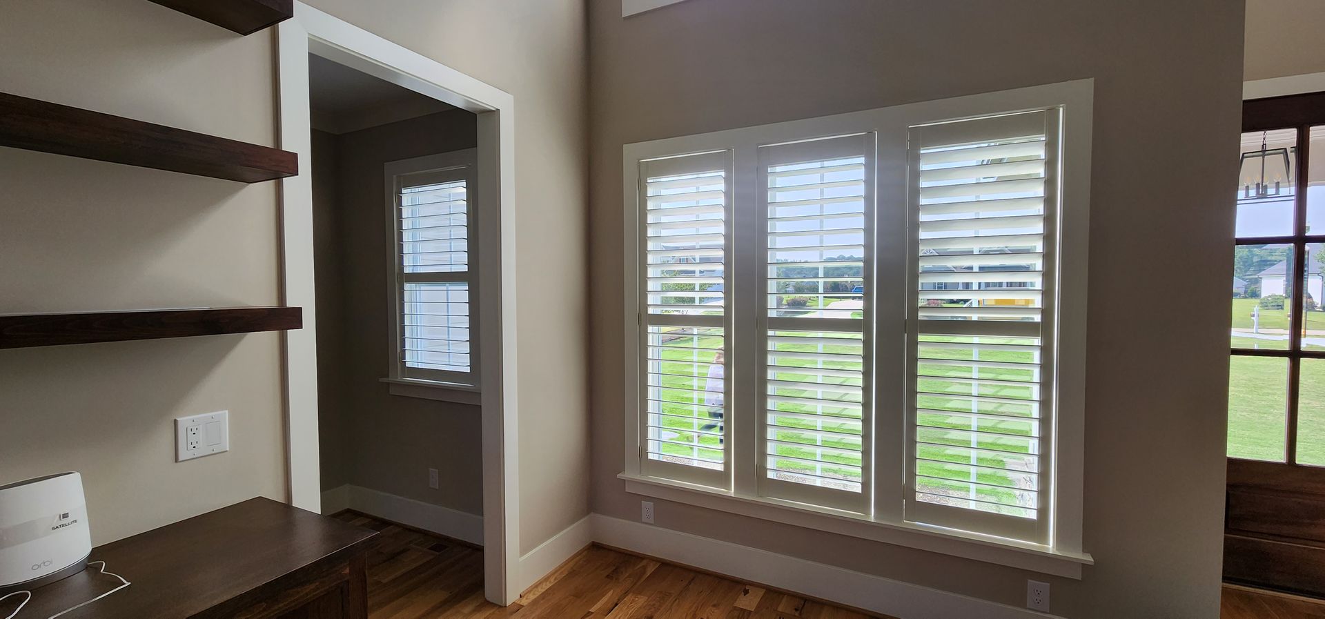 Interior room with three white shutter windows, doorway, shelving and a door.