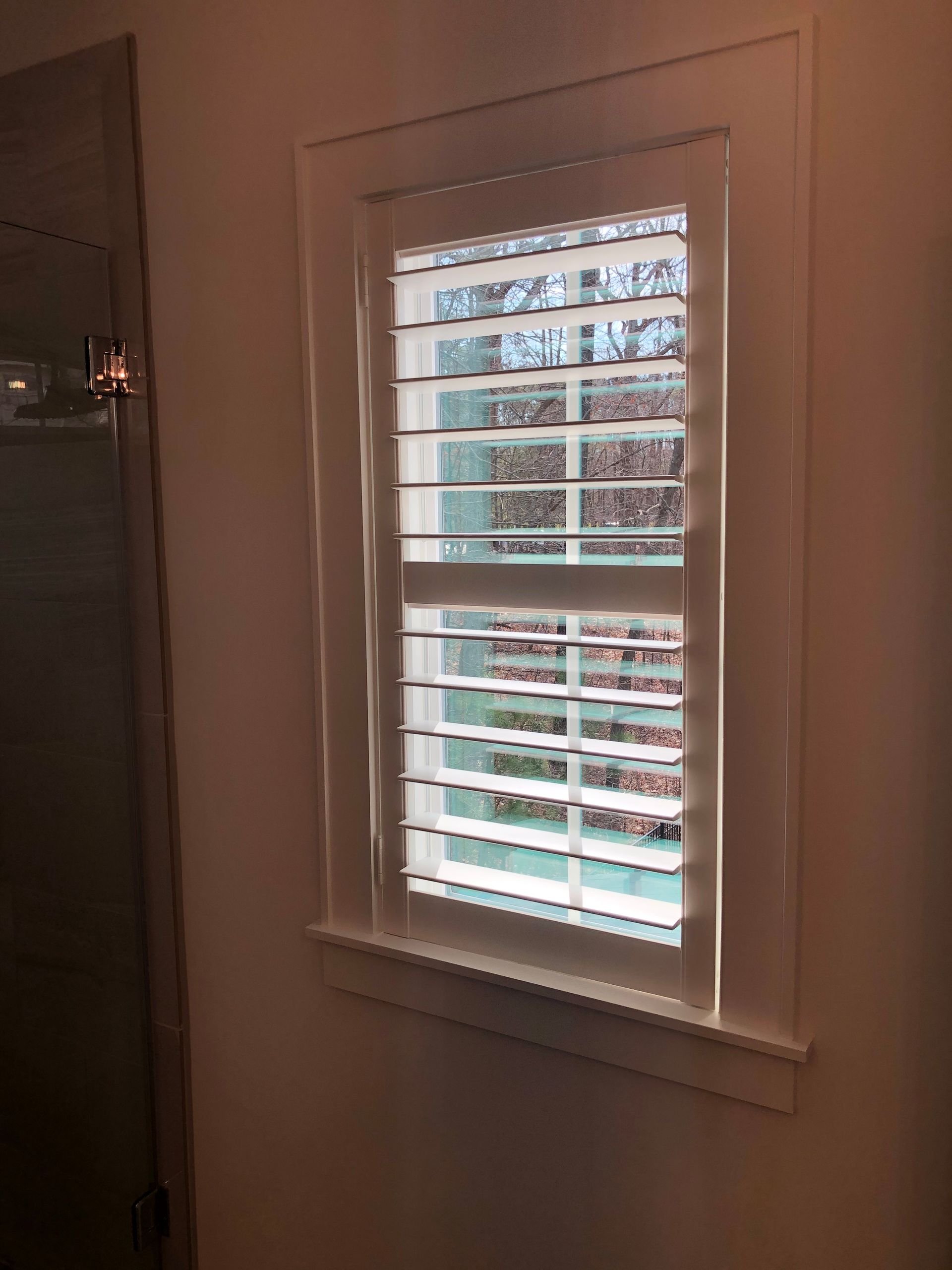 Window with white shutters and trim. Interior view, natural light.