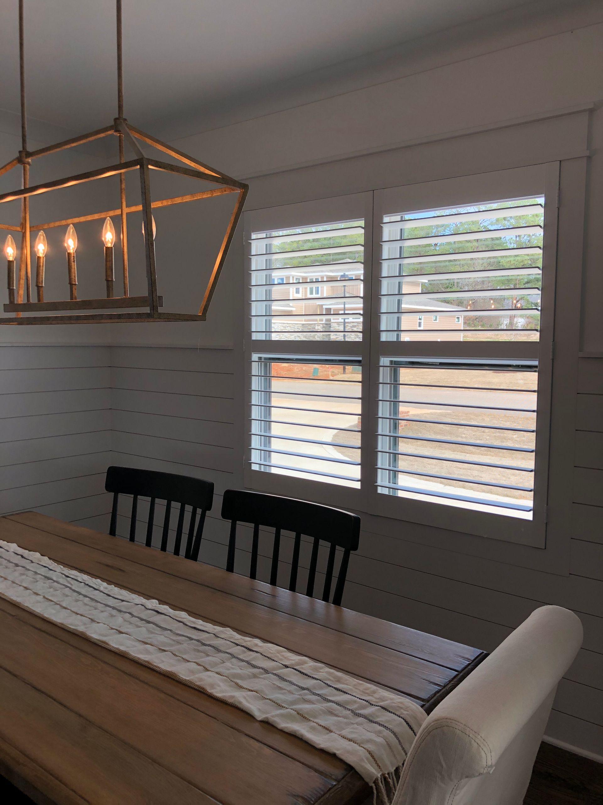 Dining room with wood table, black chairs, white shutters, and gold light fixture.