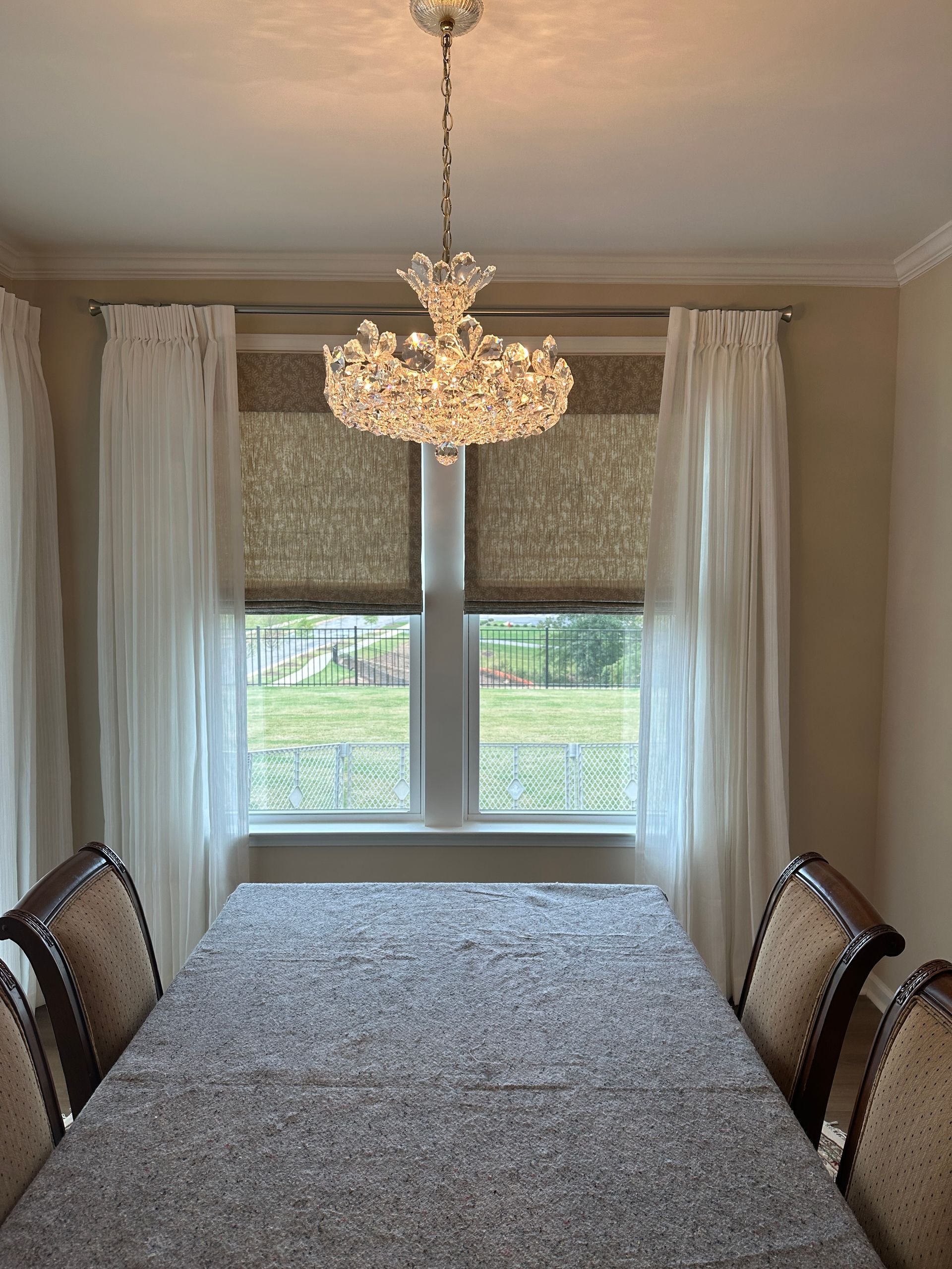 Dining room with chandelier, window, long table set with light grey cloth, six chairs.