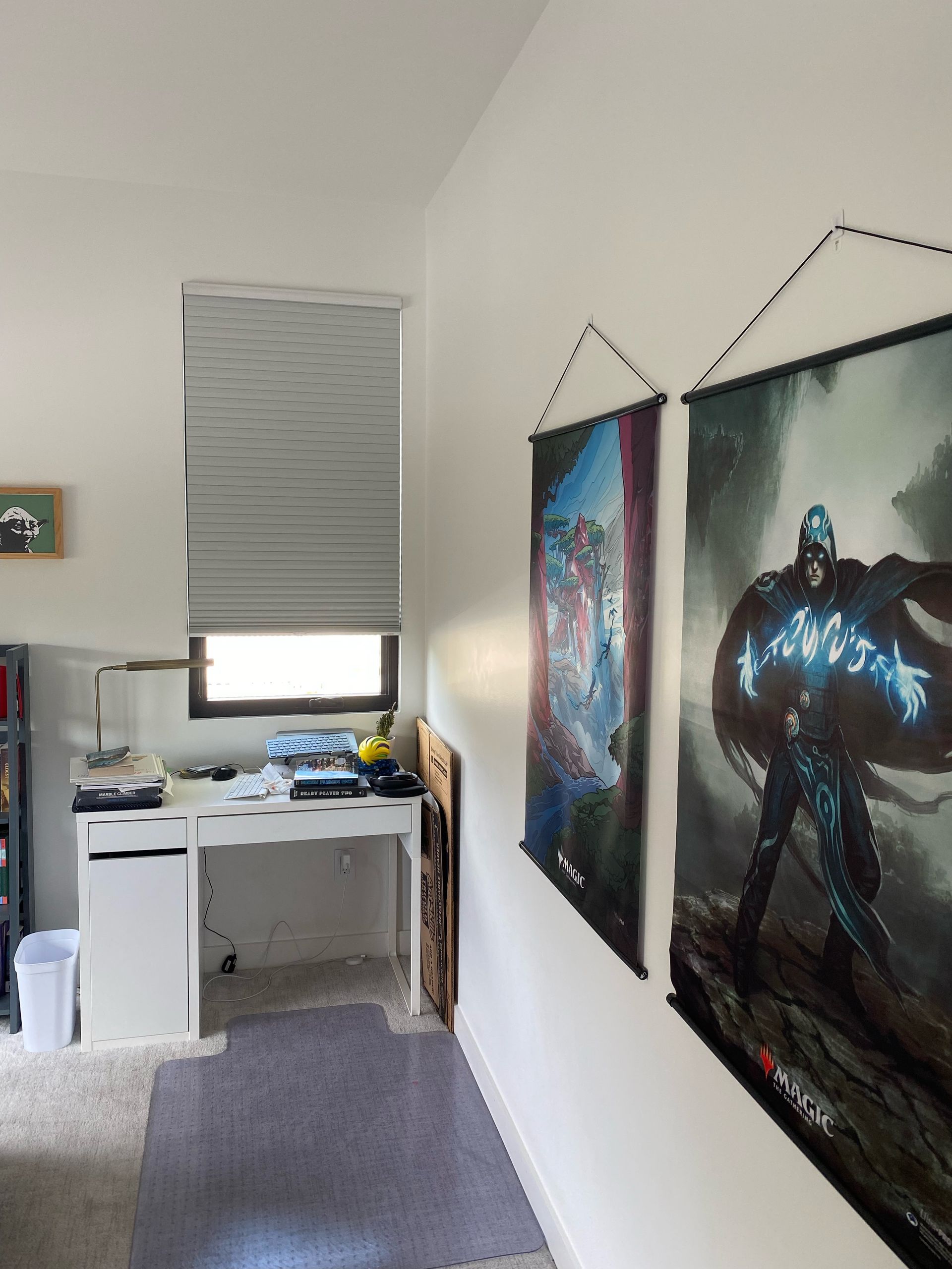 A desk with a window, two hanging posters, and a bonsai tree.