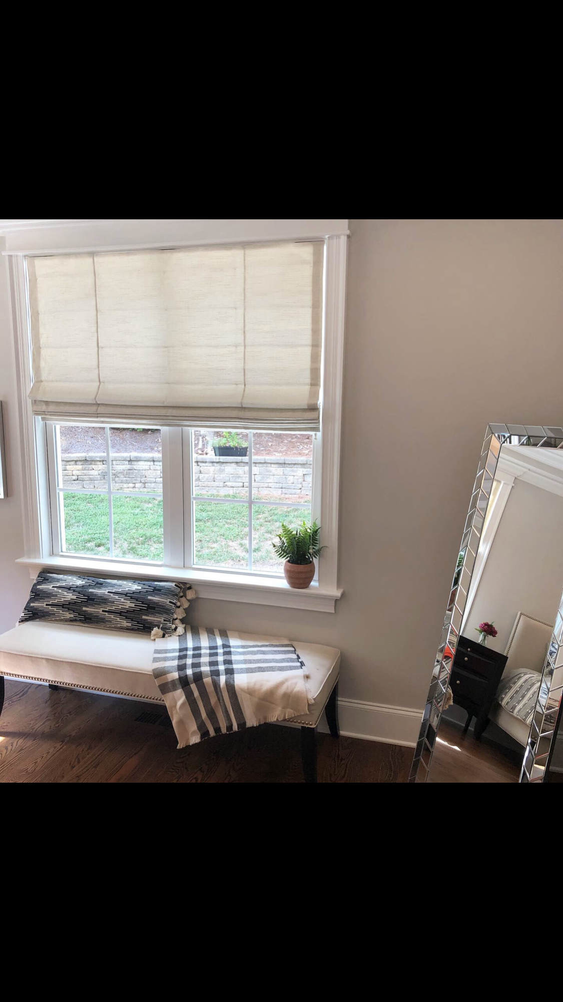 Room with window, bench, and mirror. Window has blinds, bench has pillow and blanket, mirror is ornate.