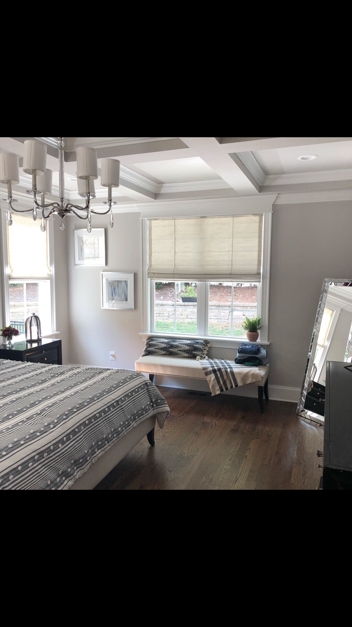 Bedroom with wood floors, a bench by the window, and a chandelier. Light walls and a patterned bedspread.