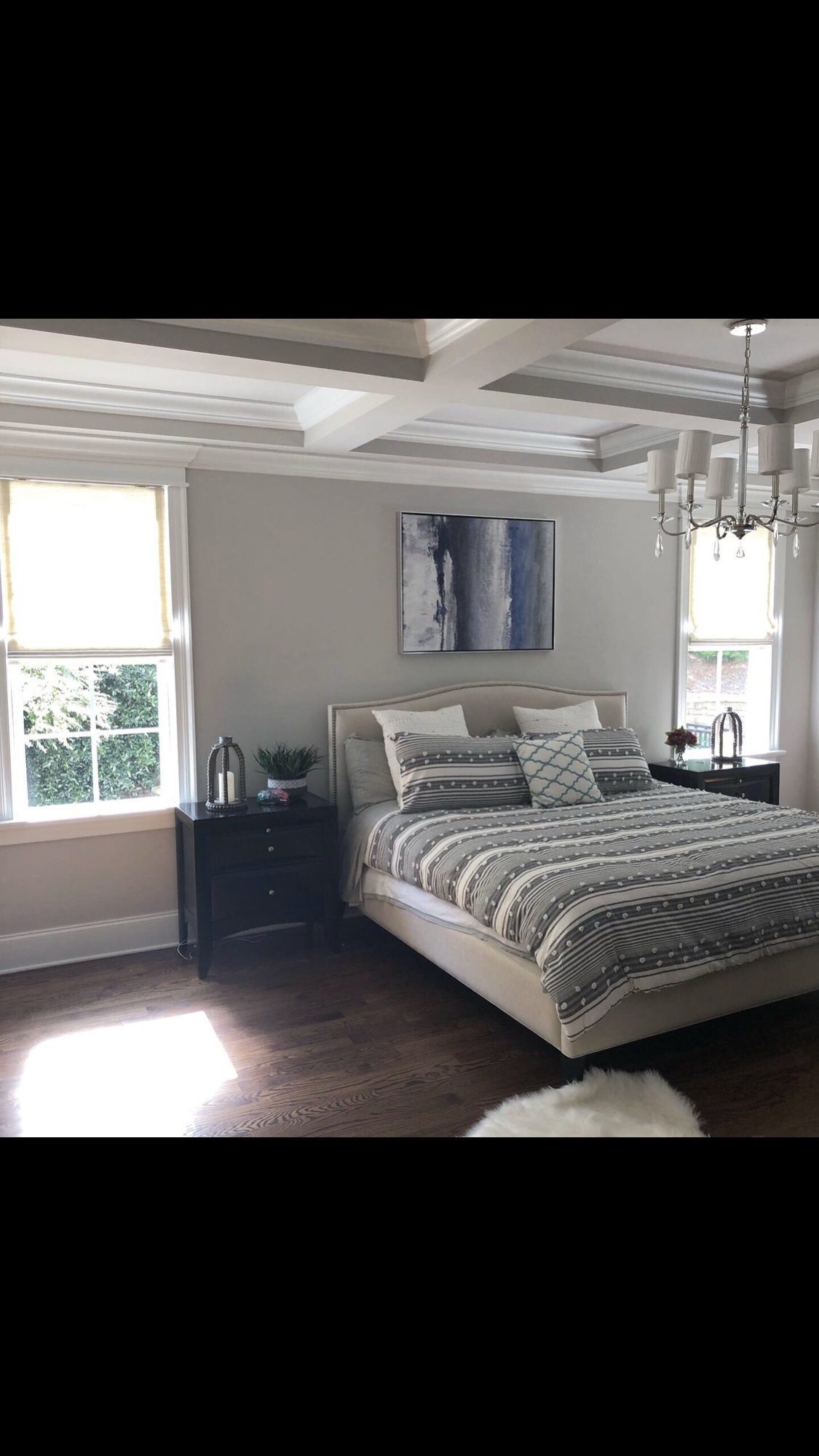 Bedroom with bed, nightstands, windows, art, and chandelier; neutral colors.