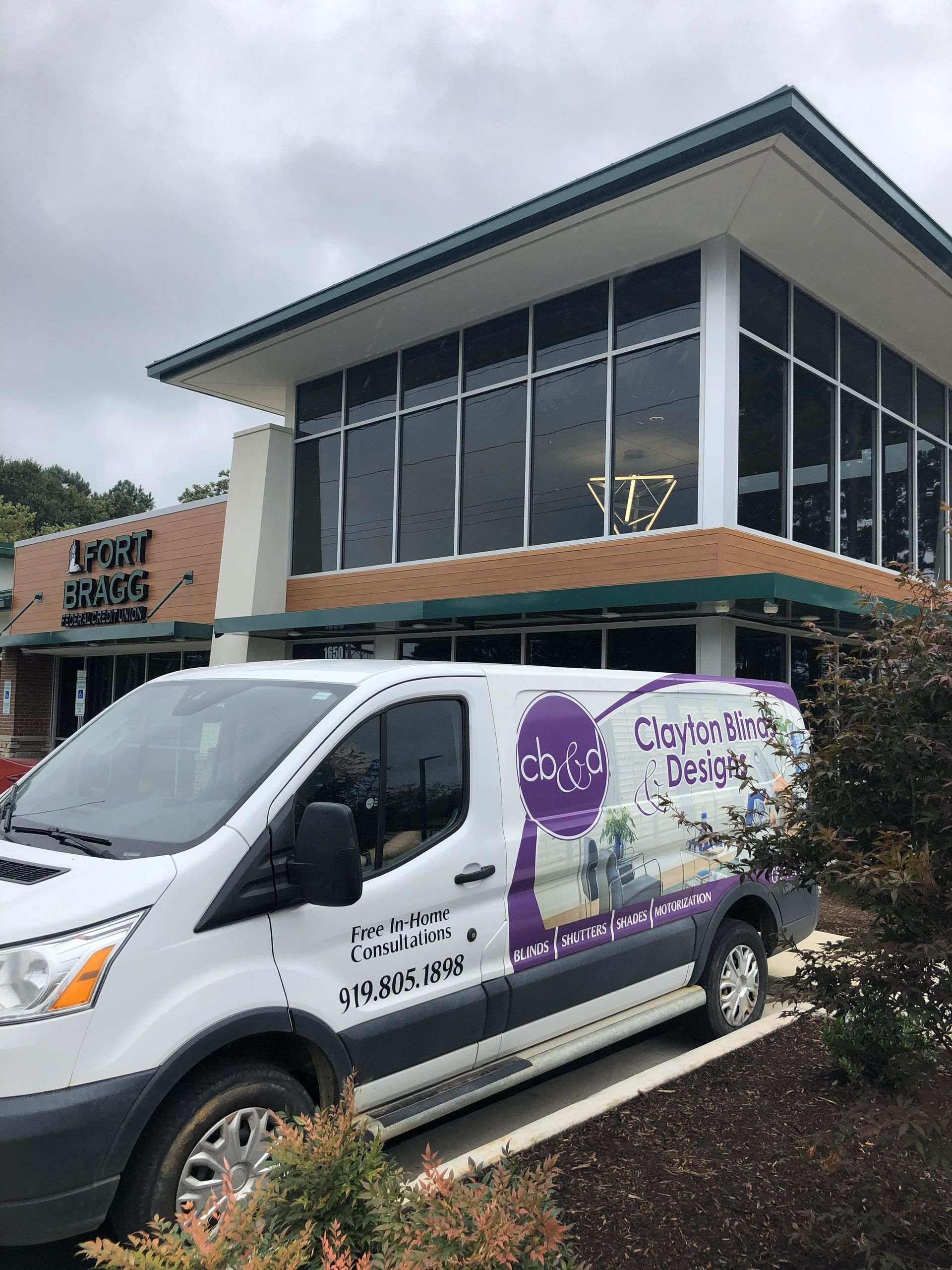 A white van with purple lettering parked in front of a building with large windows.