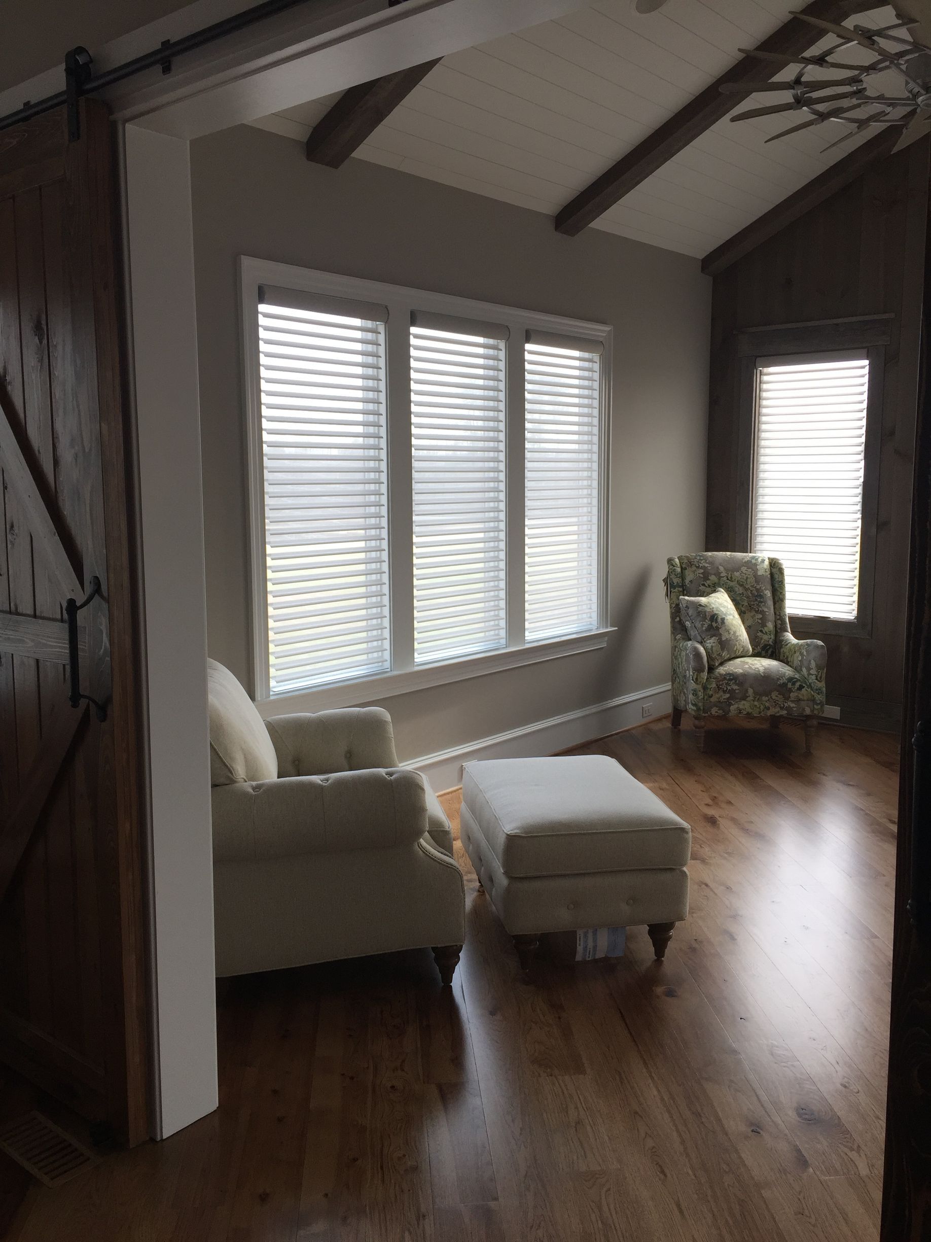 A cozy room with two armchairs, an ottoman, and a window with blinds.