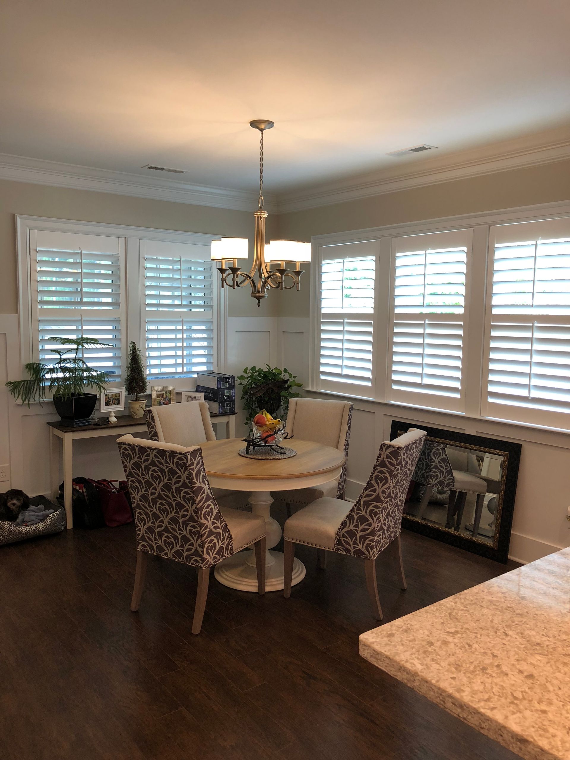 Dining room with a round table and chairs, window shutters, and a chandelier.