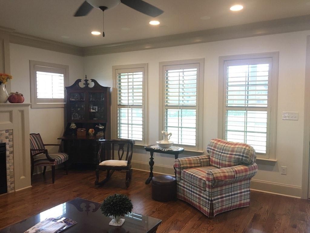 Living room with wooden floors, shutters, and furniture: chair, hutch, rocking chair, and a plaid armchair.