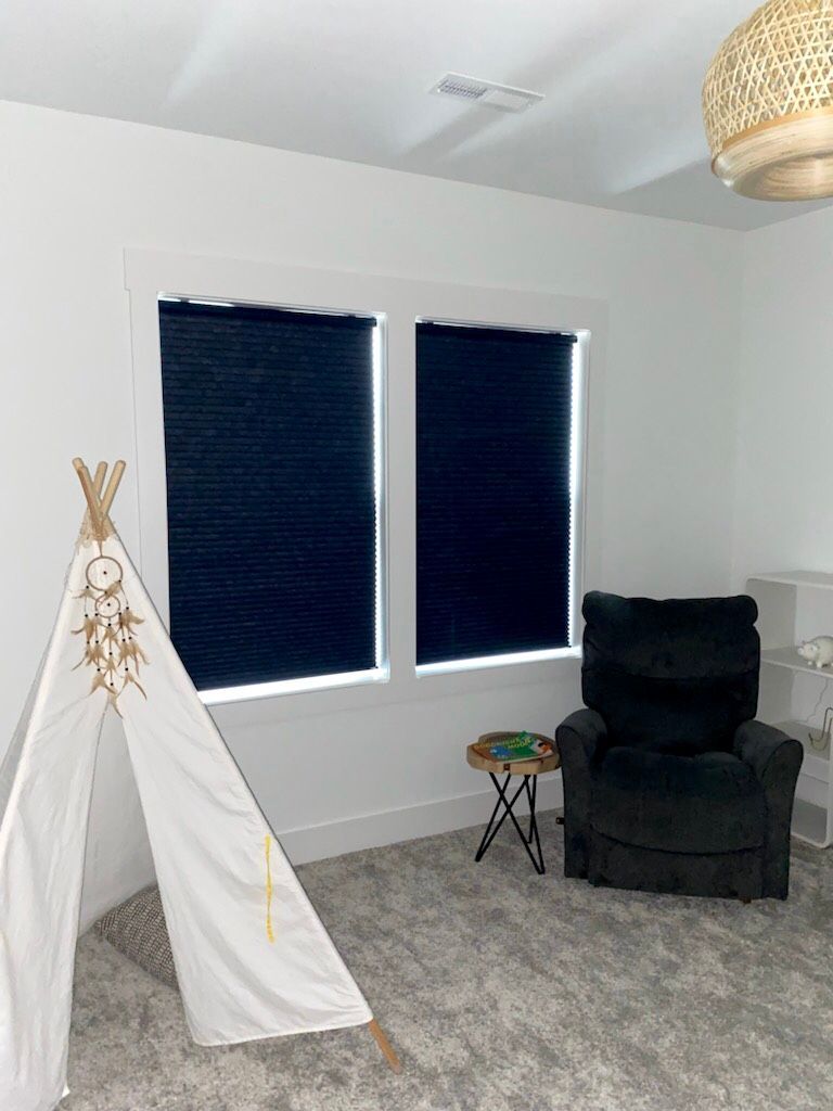 Child's room with white walls, black blinds, a teepee, and a dark recliner.