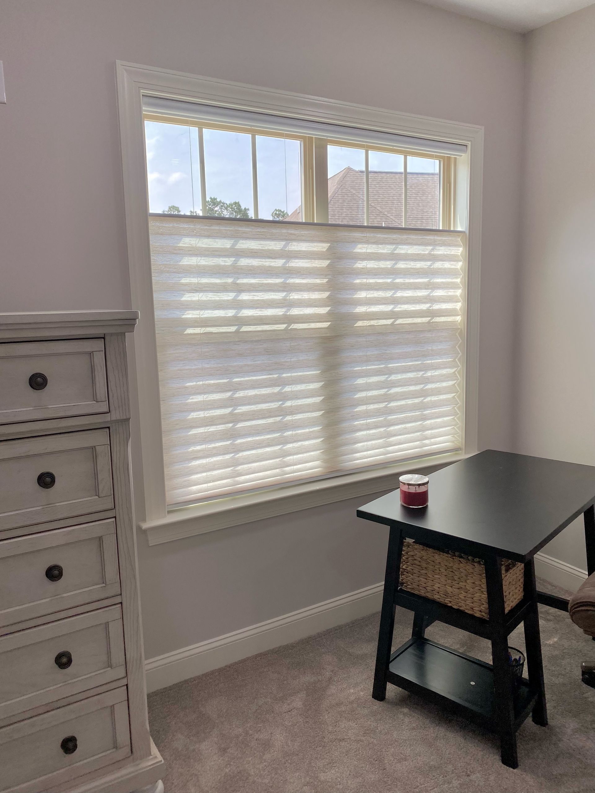 Room with a window, white blinds, dresser, and a black desk. Soft gray walls and carpet.