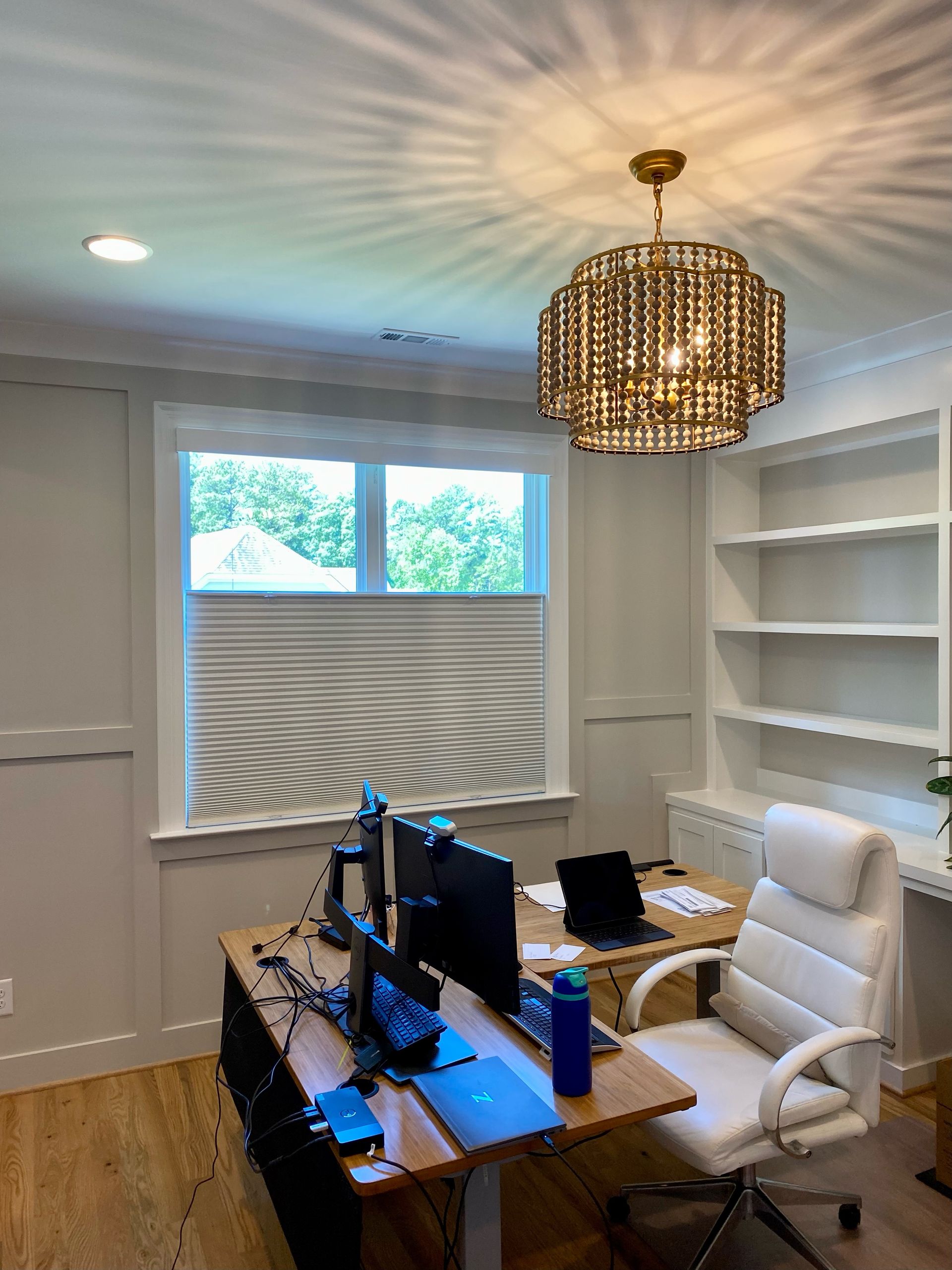 Home office with a desk, window, bookshelves, and decorative light fixture.