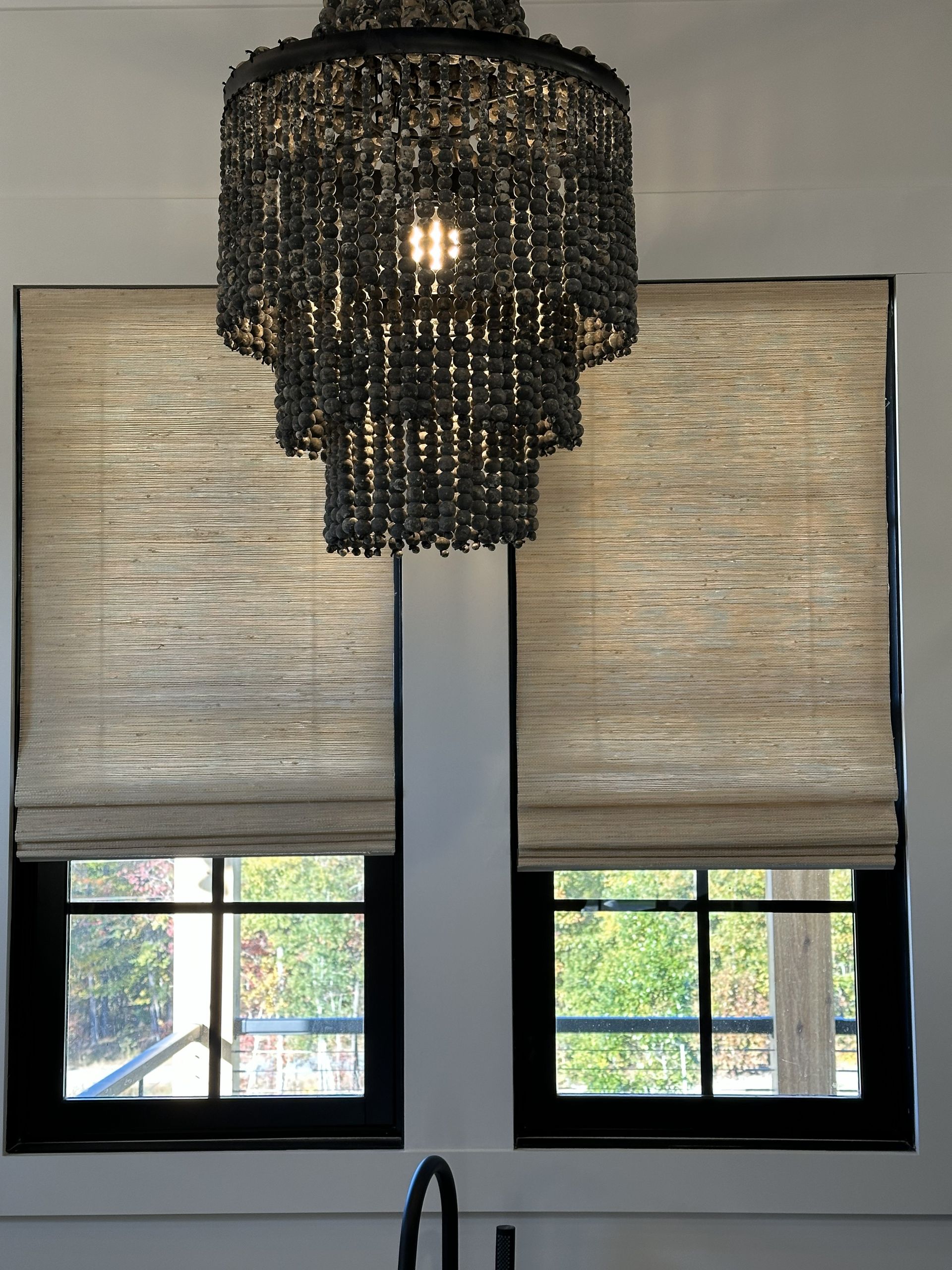 Two windows with tan shades, a dark chandelier, and black window frames.