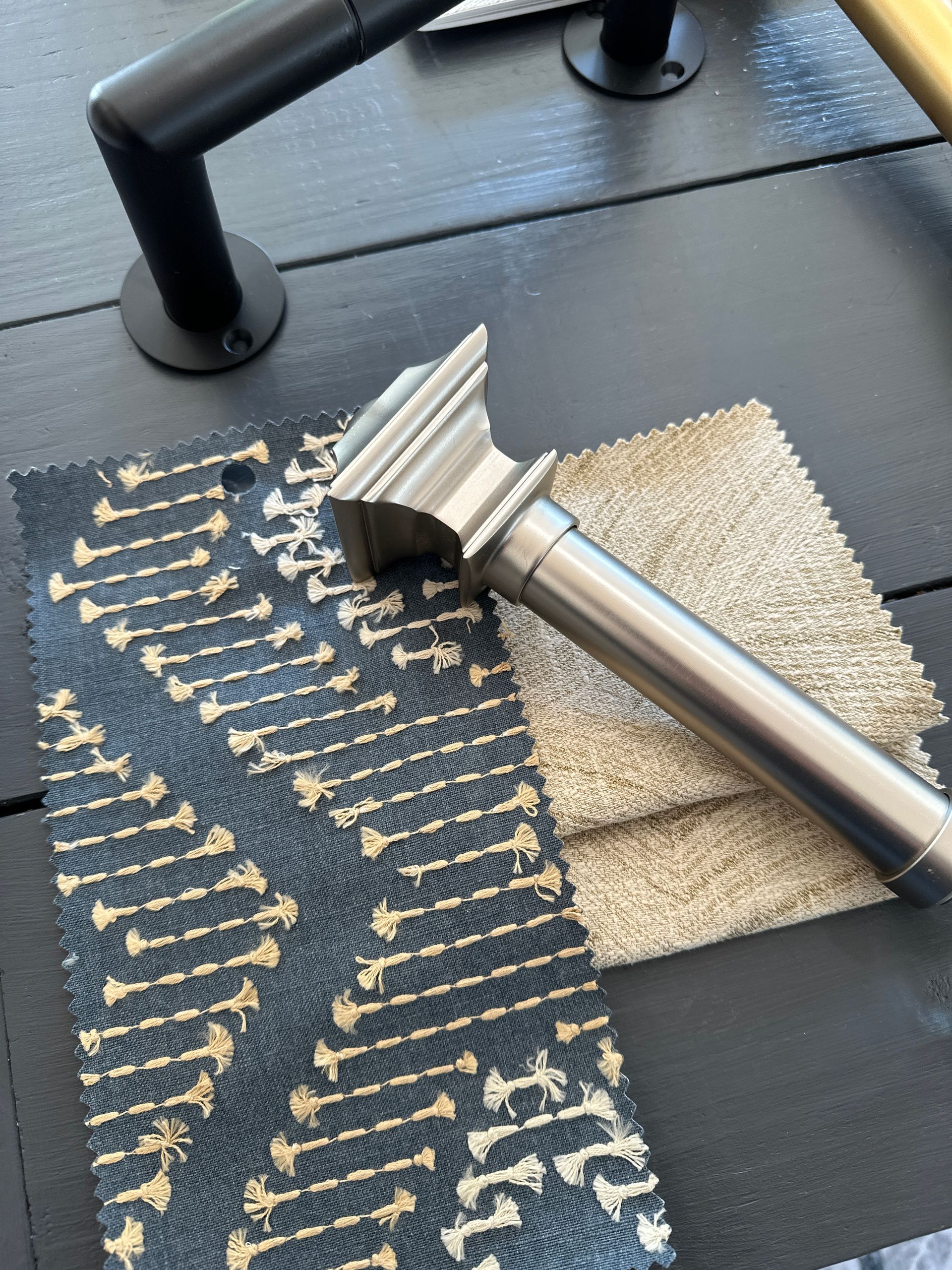 Close-up of fabric swatches, a silver curtain rod, and black curtain rod hardware on a dark wood surface.