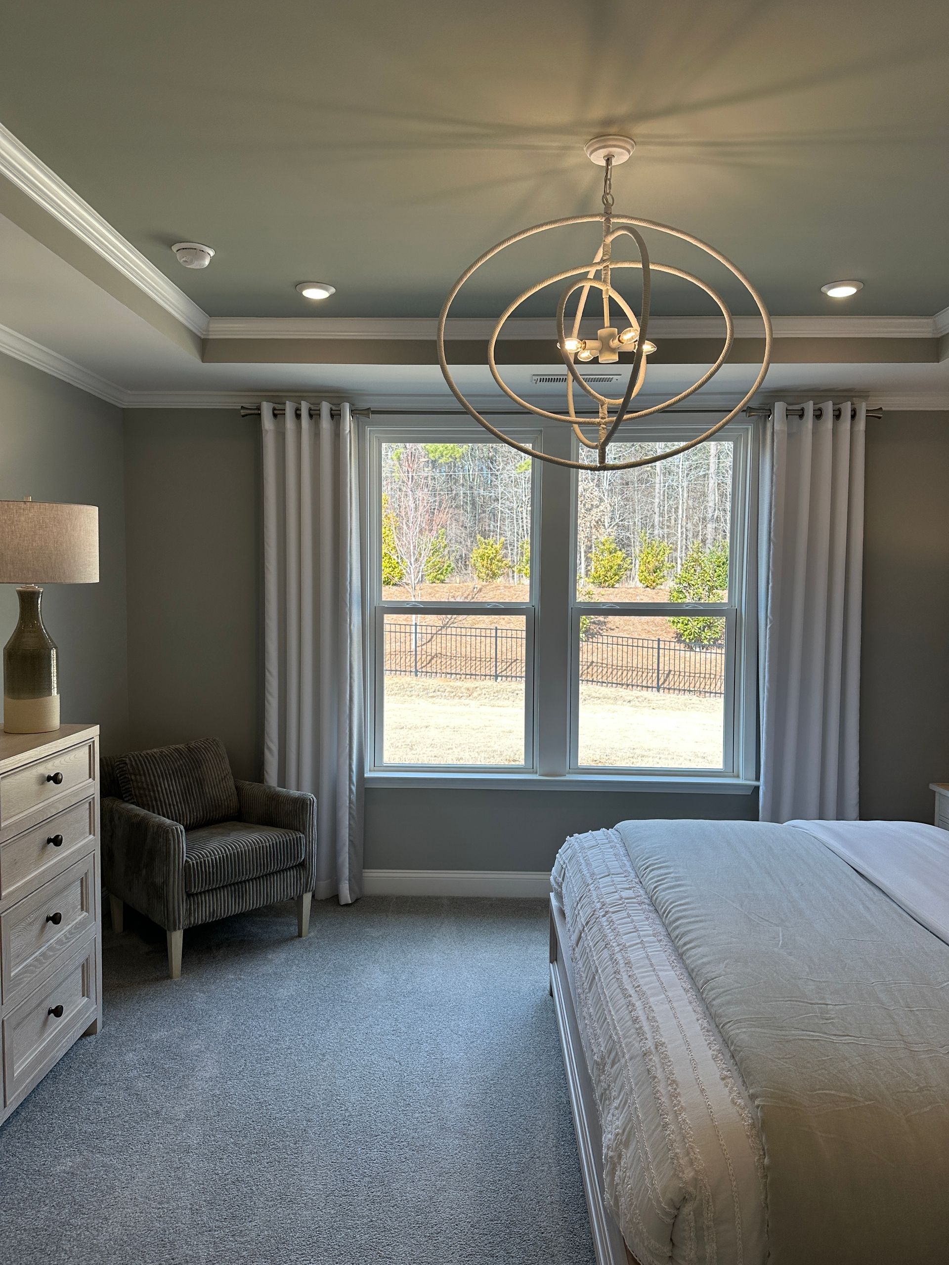 Bedroom with gray walls, window, white curtains, gray carpet, and chandelier.