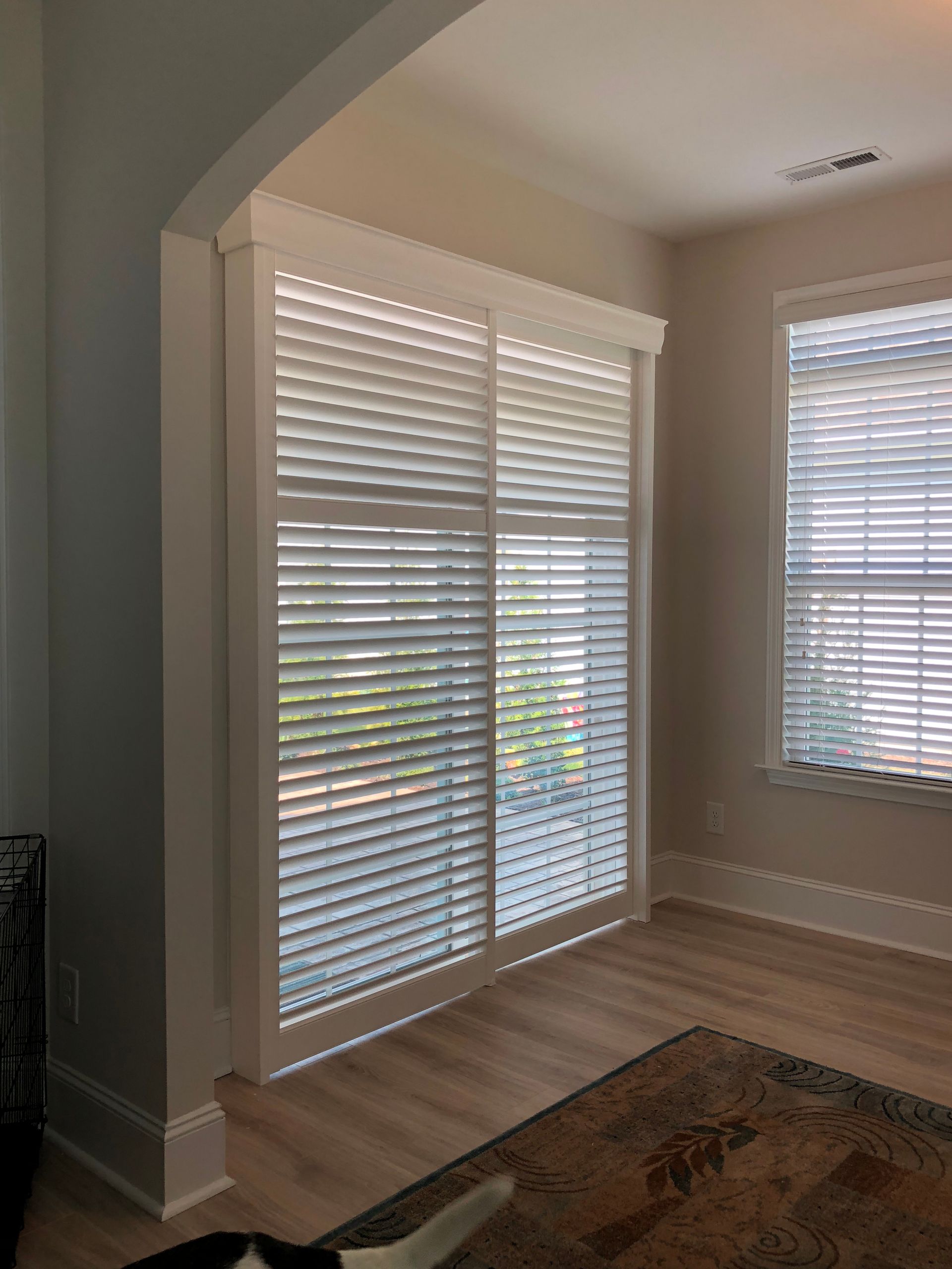 White shutters cover a sliding glass door and a window. Light wood floor and a patterned rug.
