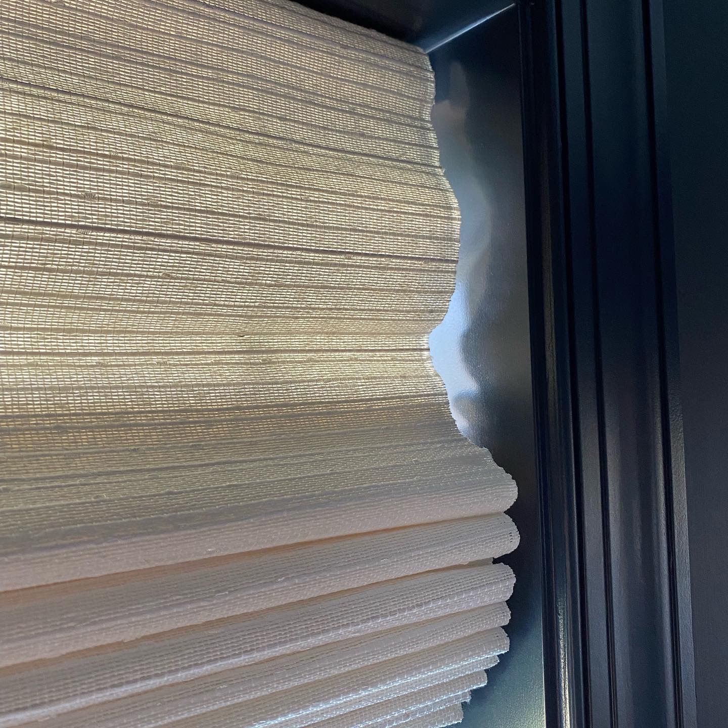 Beige roman shade partially open, revealing window and frame.