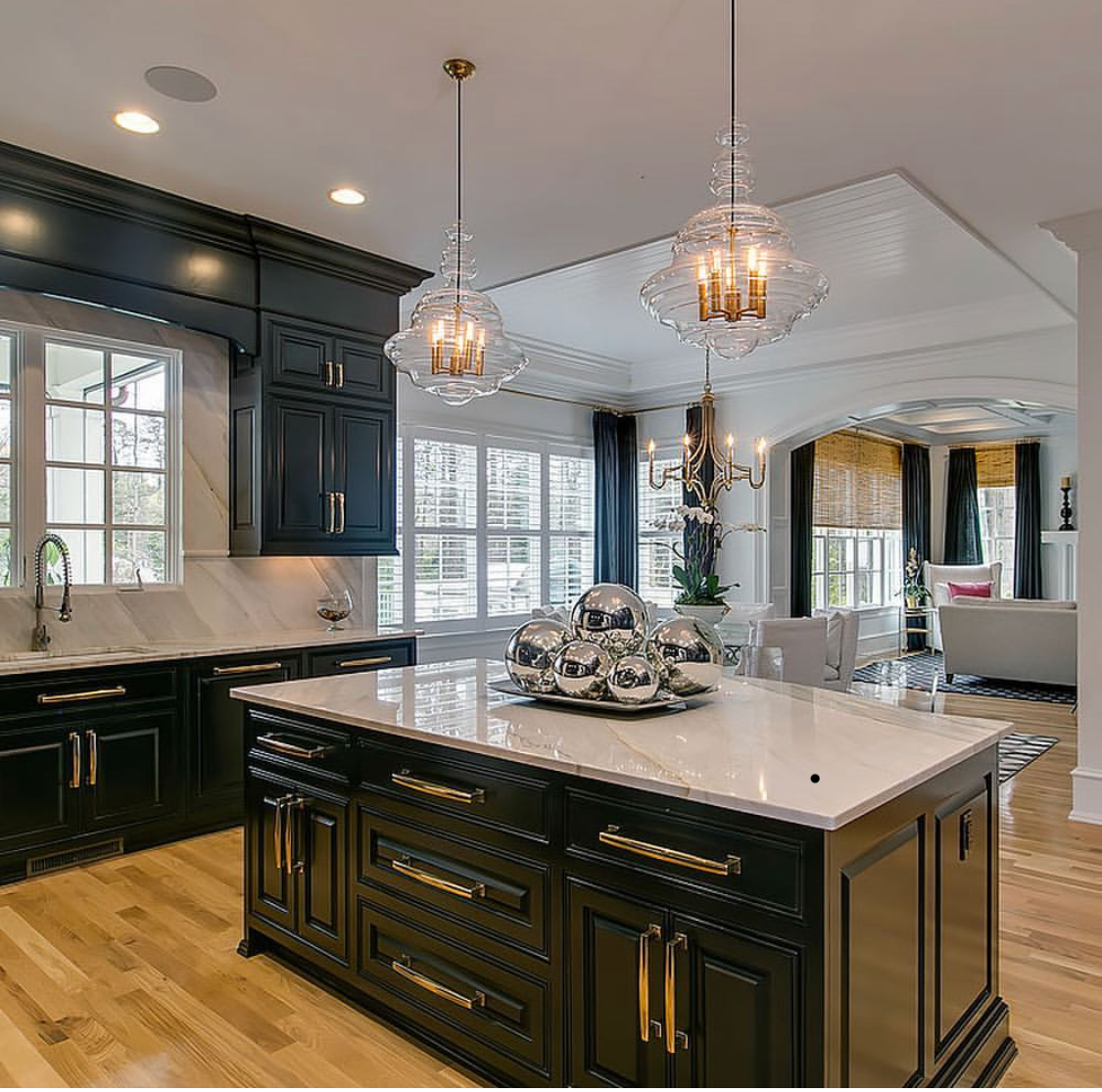 Elegant kitchen with black cabinets, white countertops, island, and decorative light fixtures.
