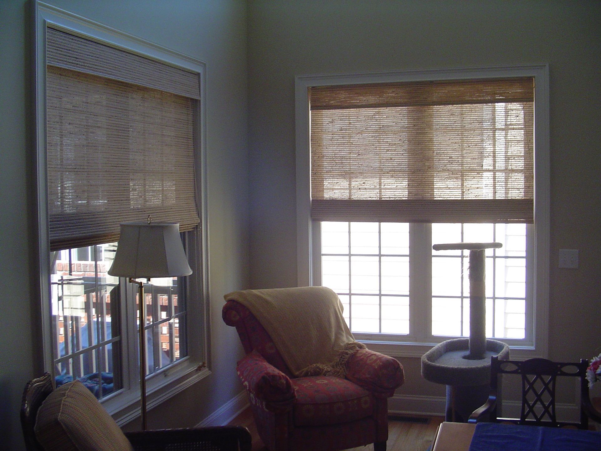 A room with two windows covered by woven shades, a red chair, a floor lamp, and a cat tree.