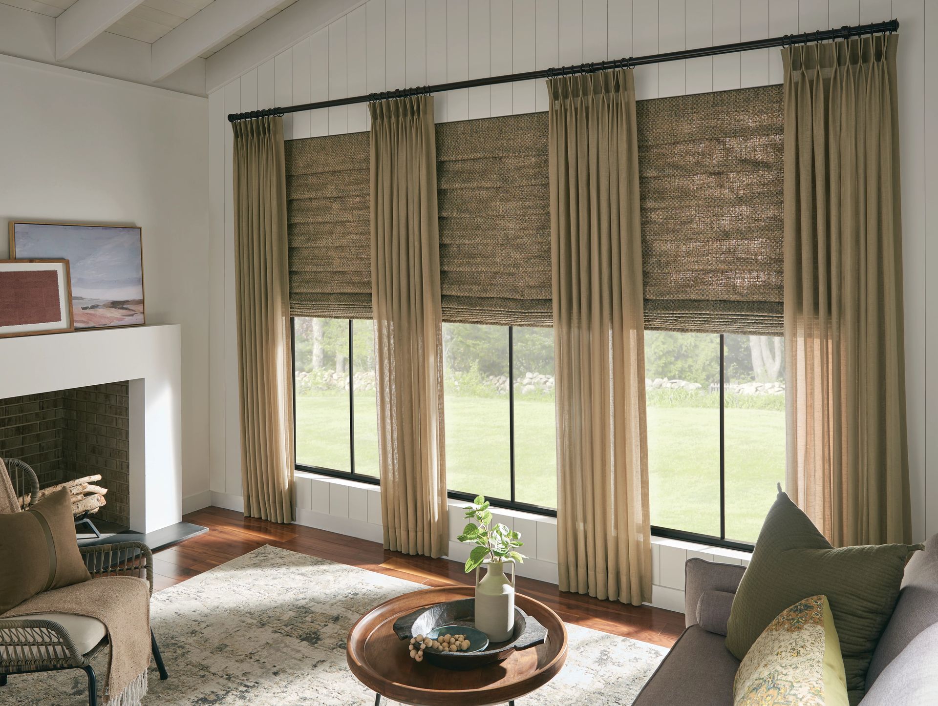 Living room with three tall windows; tan curtains, woven shades, and a fireplace.