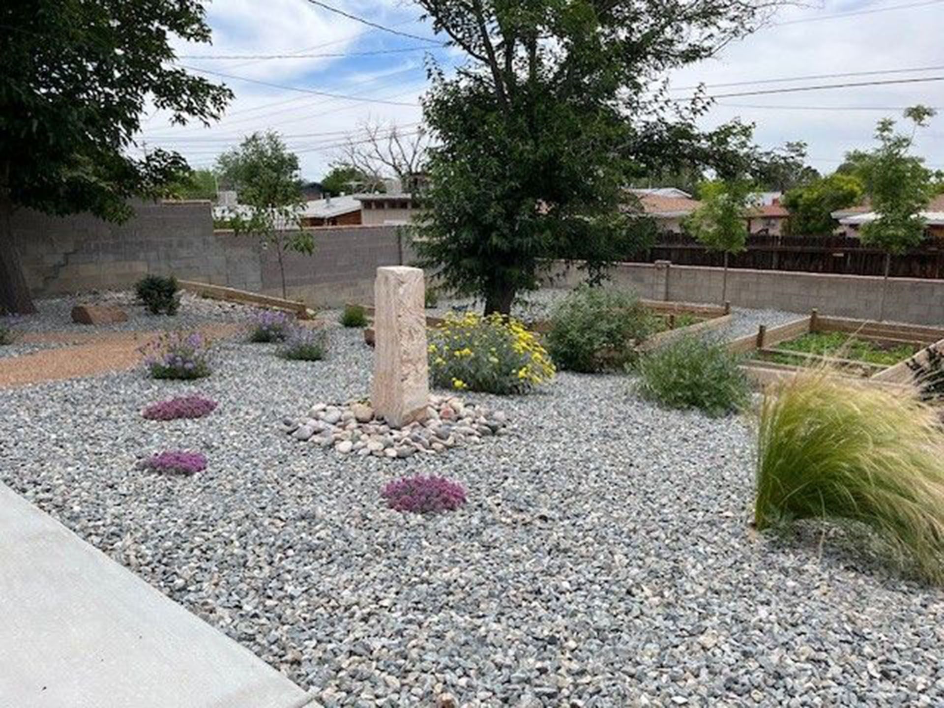 A gravel garden with flowers and a fountain in the middle.