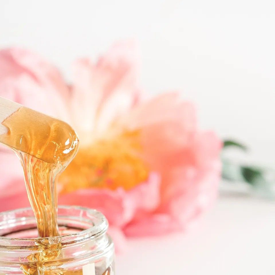 Wax dripping from a wooden stick into a jar; pink flower in the background.