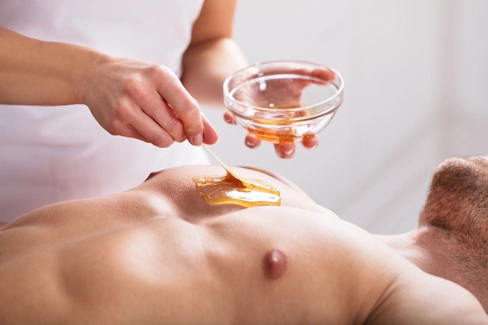 Person applying wax to a man's chest in a spa-like setting, preparing for hair removal.