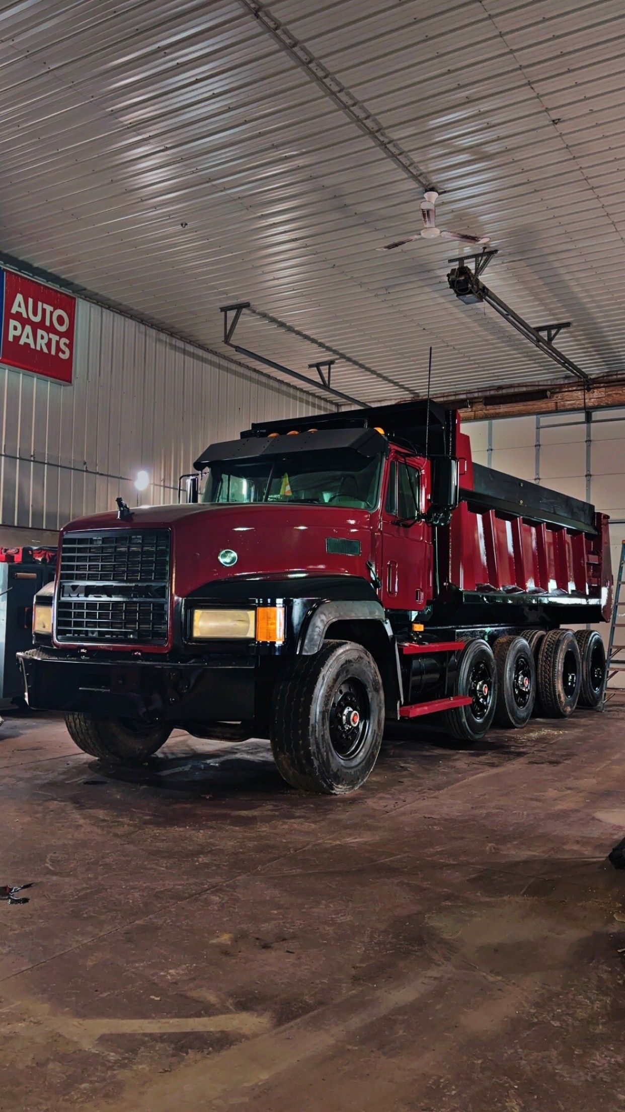 Dark red dump truck parked inside a garage with "AUTO PARTS" sign.