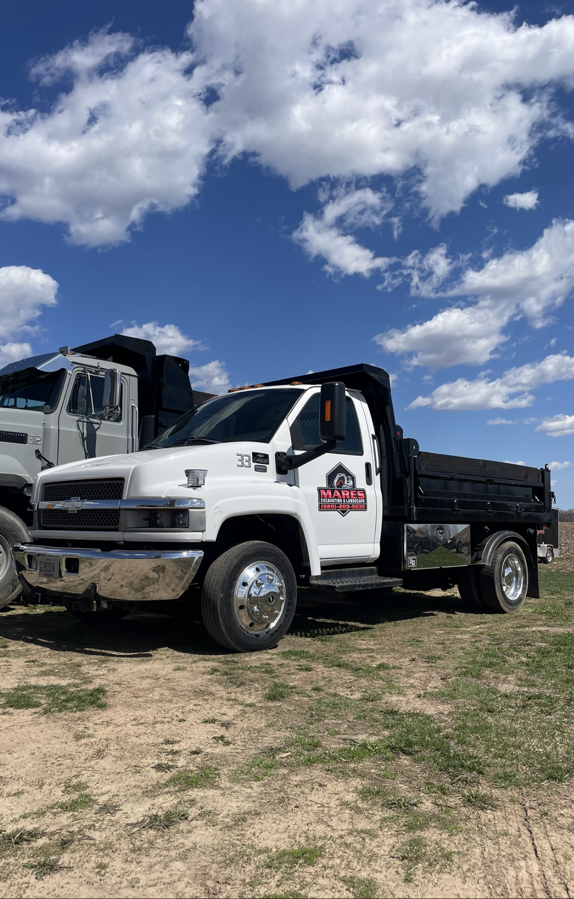 White dump truck on a field under a blue sky with clouds.