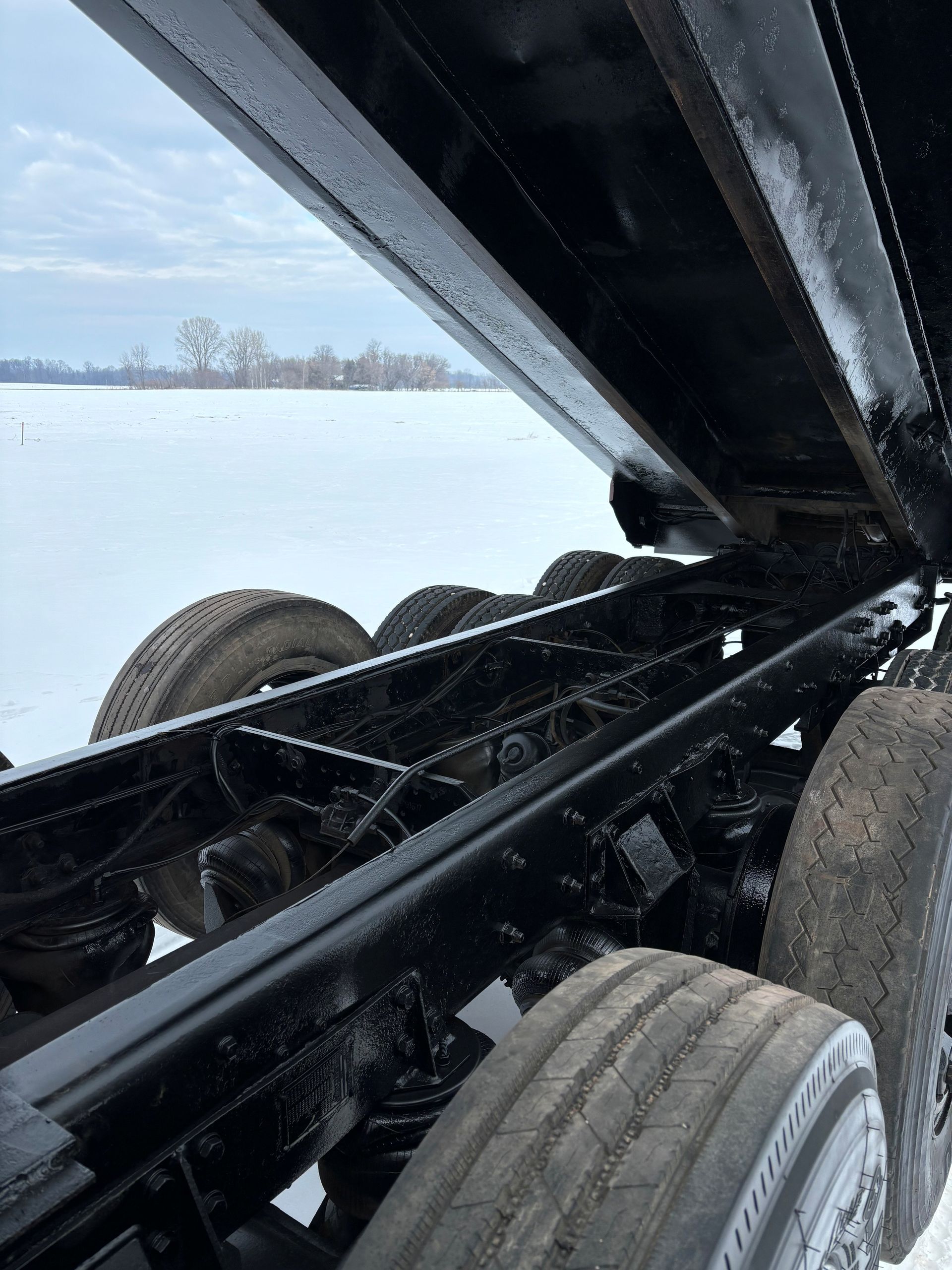 Black dump truck chassis, raised bed, on a snowy landscape.