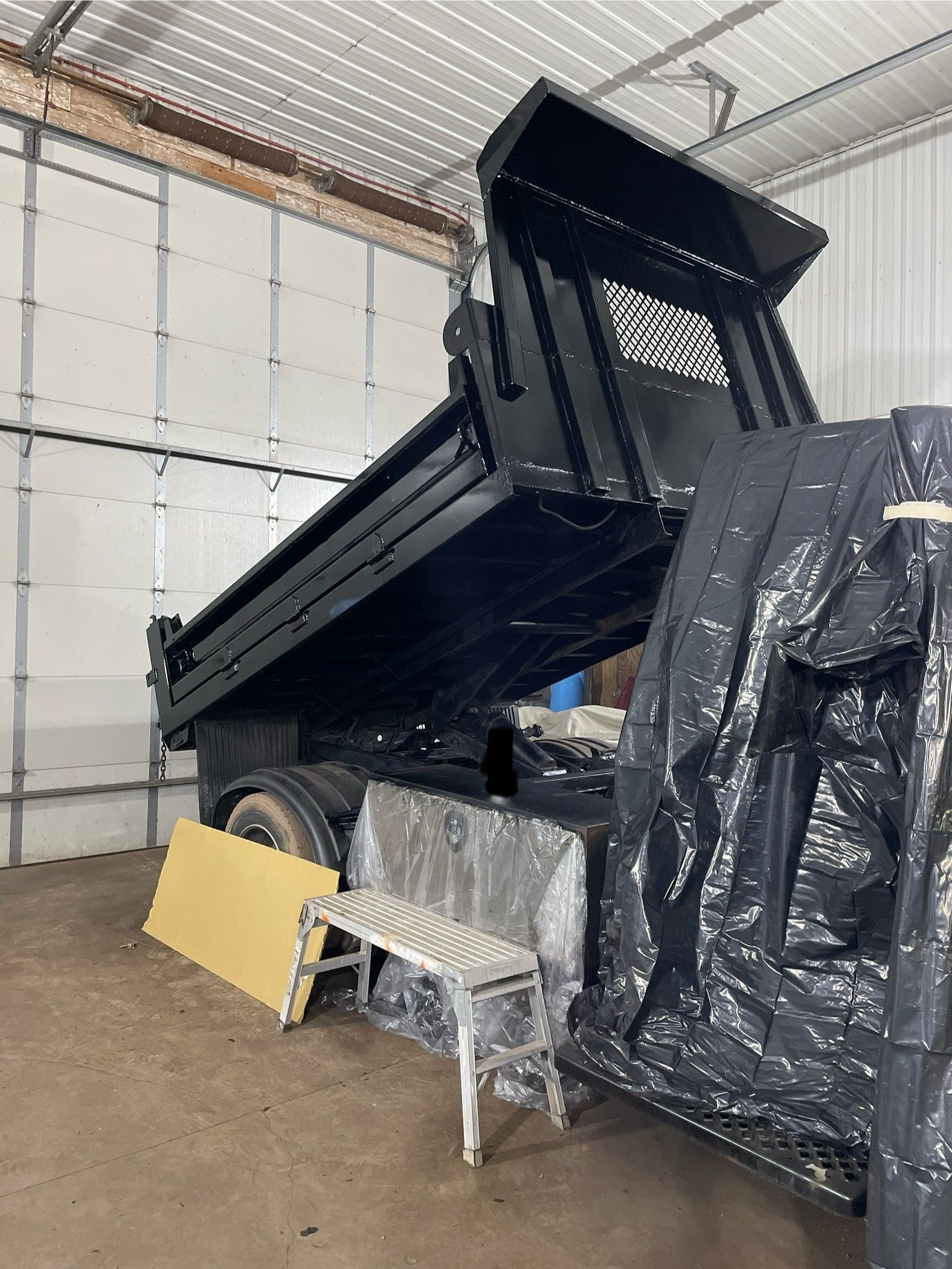 Black dump truck with bed raised inside a garage.