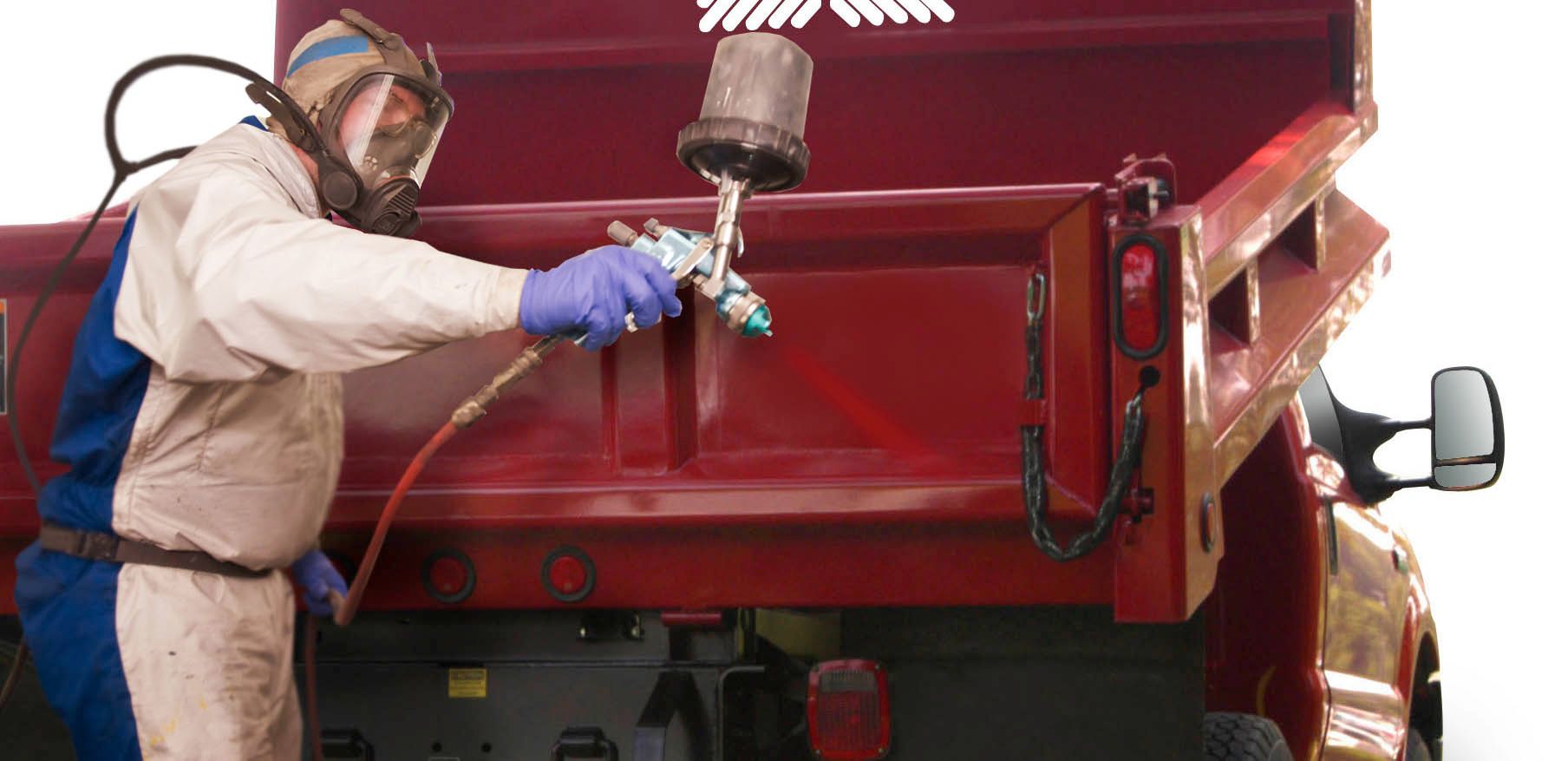 Person in protective gear spray-painting a red truck bed.