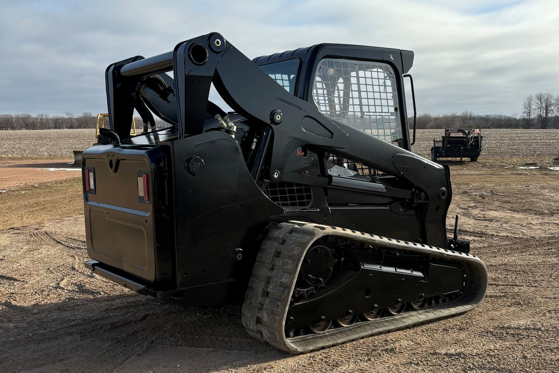 Black track skid steer on a gravel surface, in an outdoor setting.