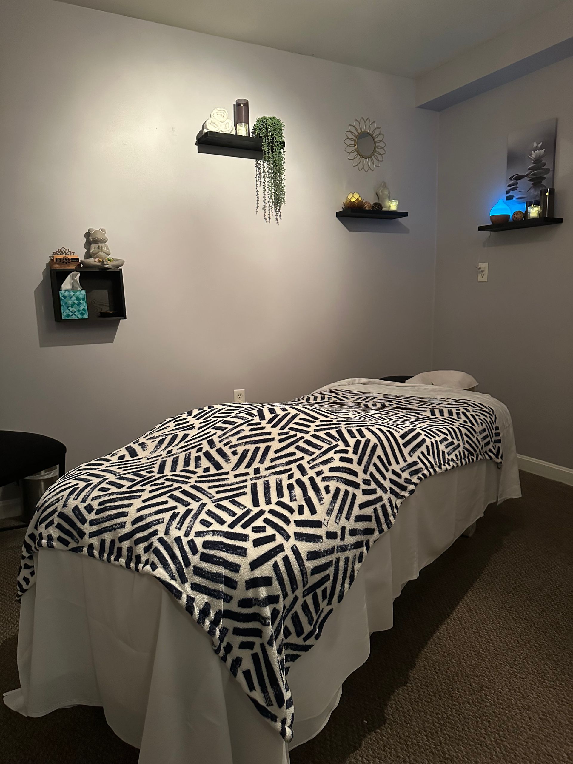Massage room with massage table, shelves with decor, and gray walls.