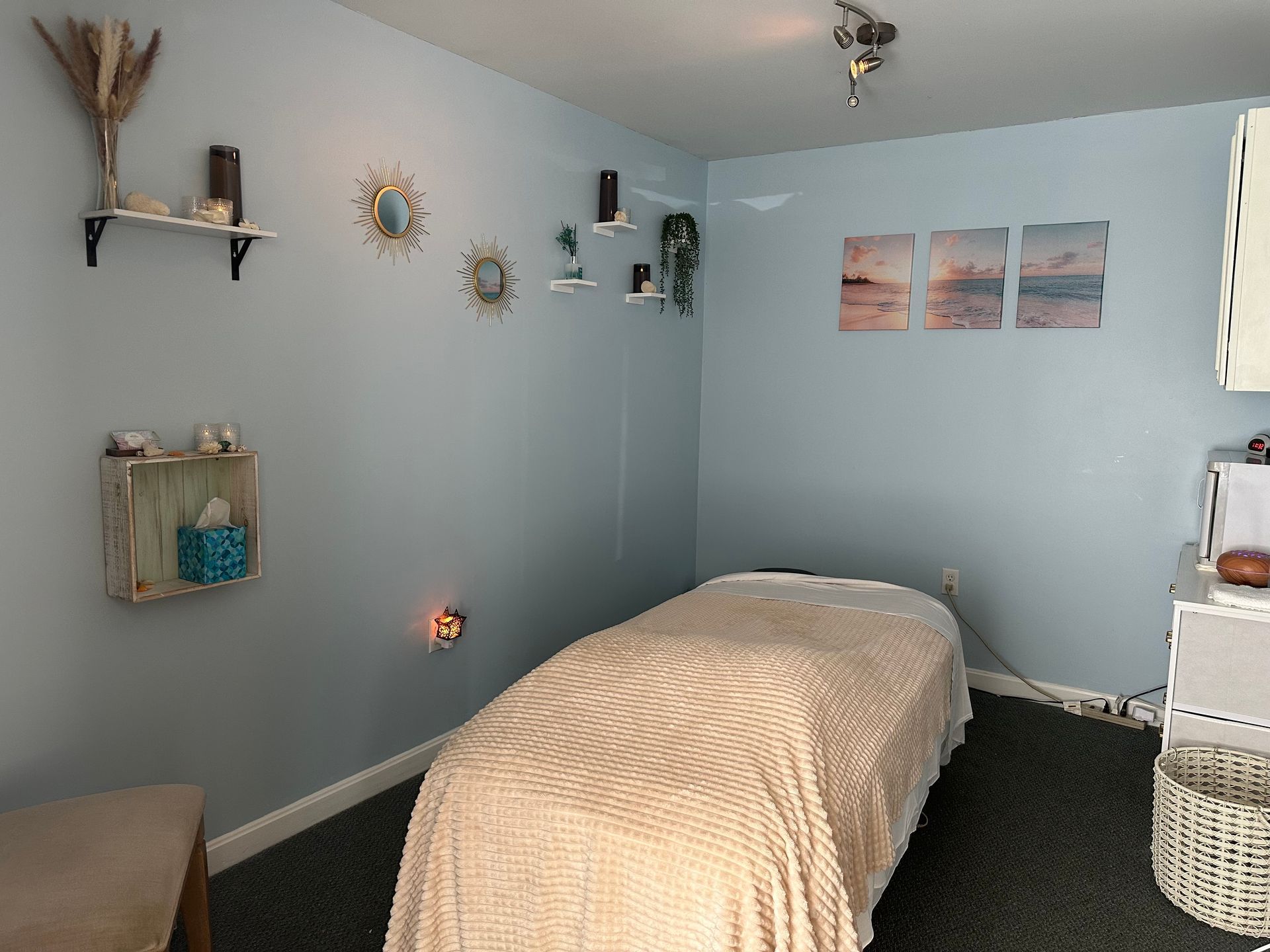 Massage room with a light blue wall, massage table, and decorative shelves.
