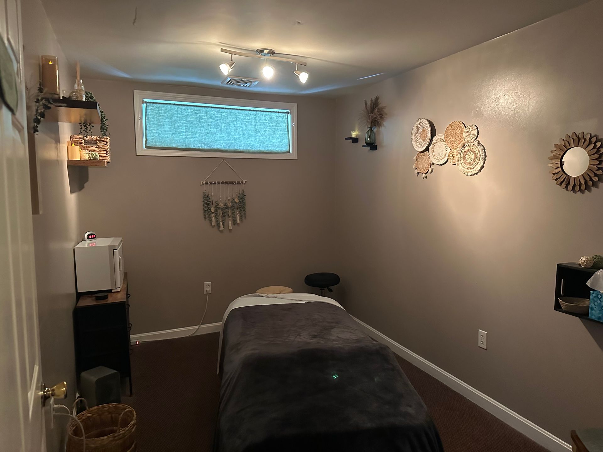 Massage room with massage table, decor, and window. Walls are brown.