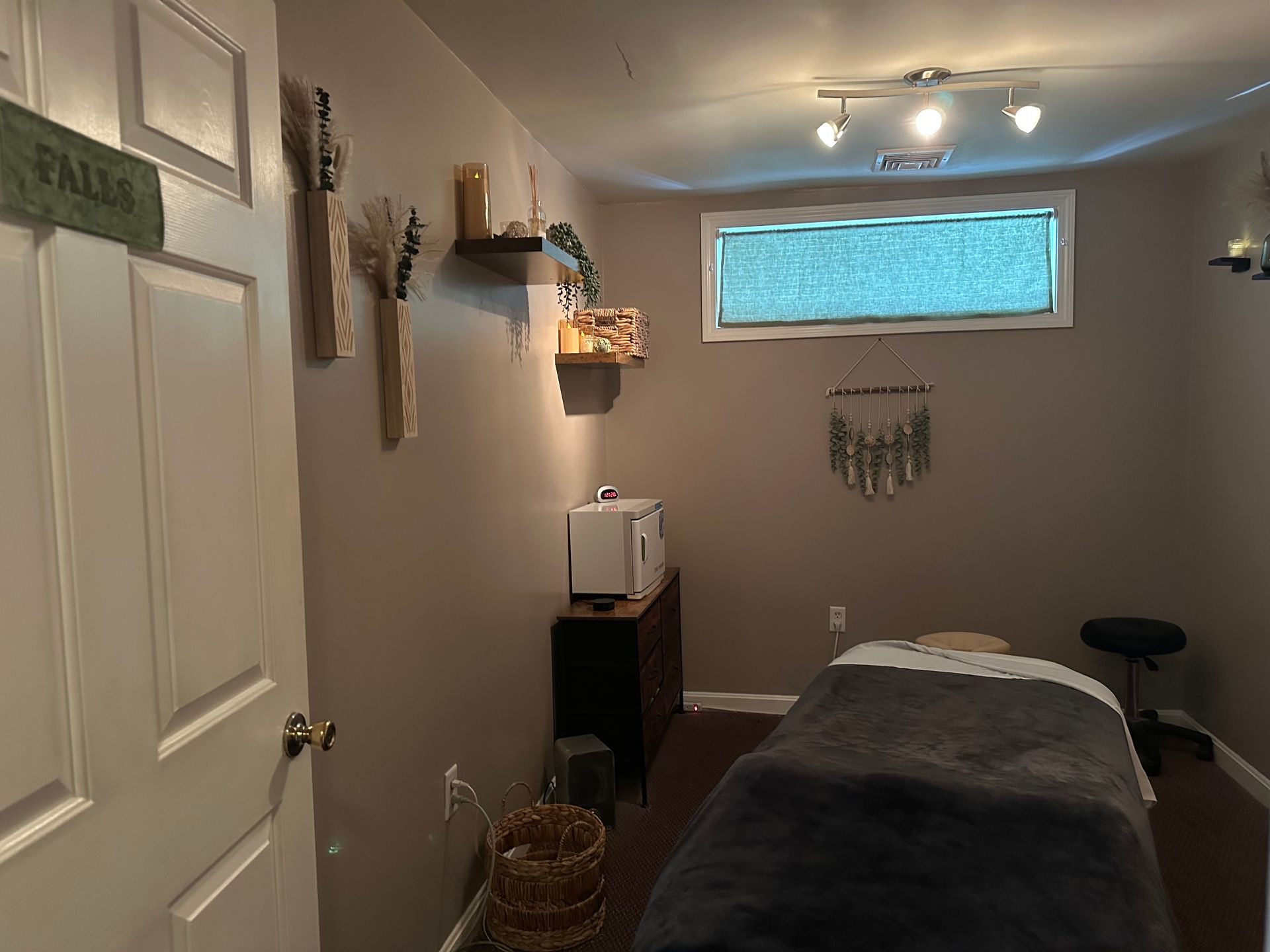 Massage therapy room with massage table, decor, and small window.