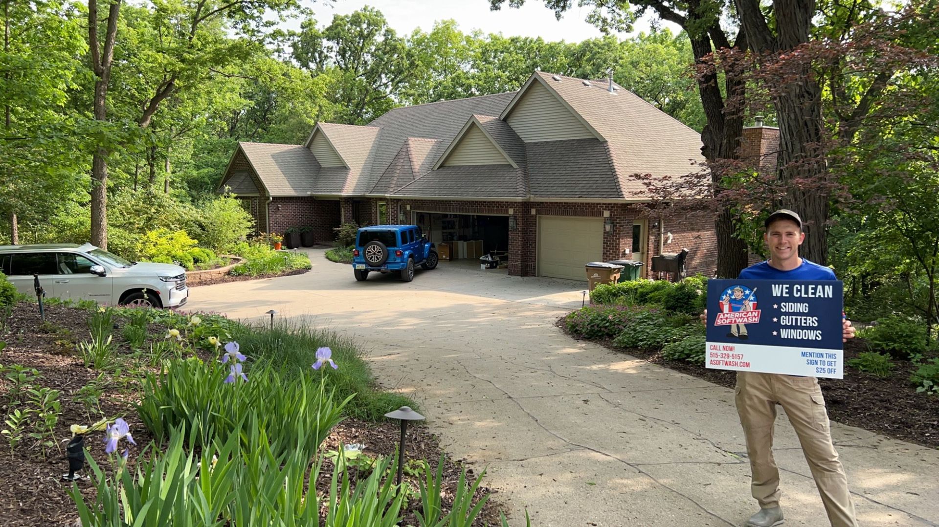 Man holding a blue real estate sign in front of a brick house with a driveway and trees