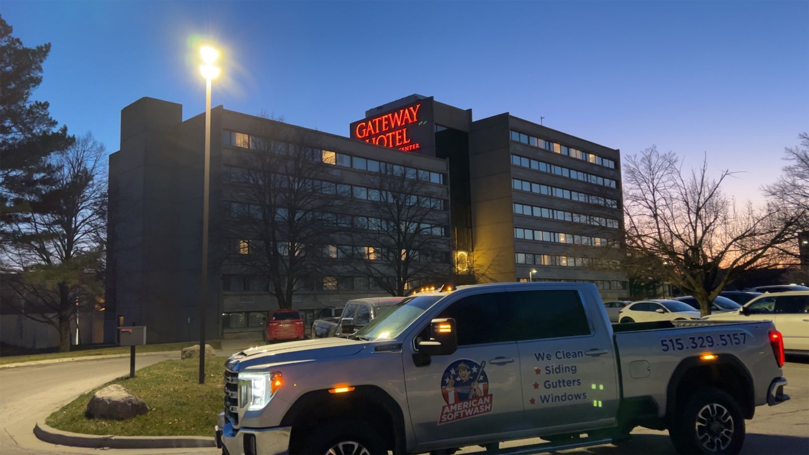 Truck parked outside a hotel at dusk, with a lit sign and bare trees in the background