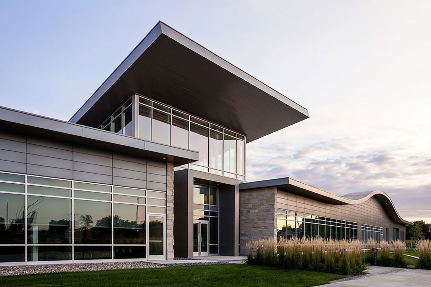 Modern glass-and-stone building with large windows and a prominent overhanging roof